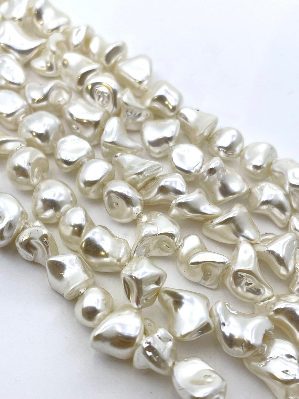 Close-up of multiple strands of irregular, polished white shell beads on a plain white background.