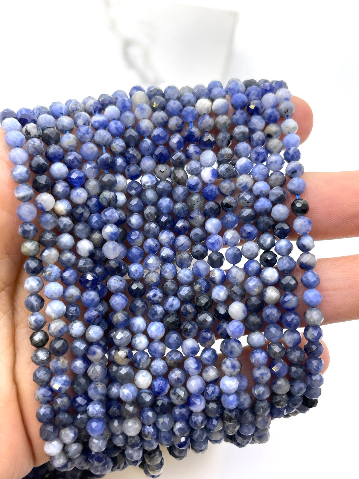 A hand holding a bundle of faceted round sodalite beads in shades of blue, navy, and white, likely selenite or labradorite.