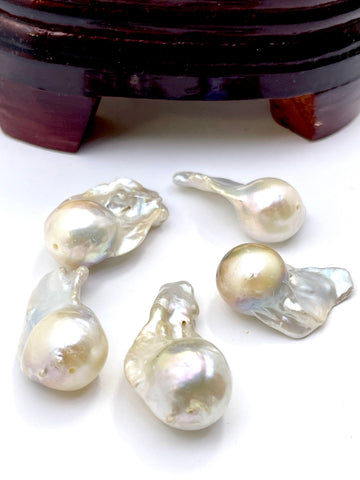 Five irregular baroque freshwater pearls with a pearlescent white and iridescent sheen, arranged on a white surface with a dark wooden stand partially visible at the top.