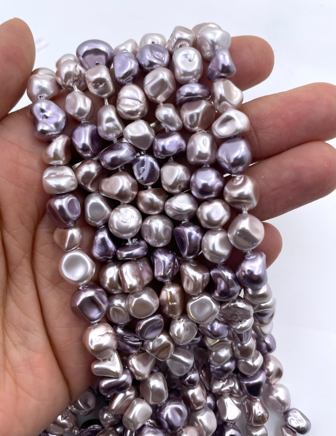 Curled strands of irregular shell pearls in a metallic lavender-gray color, displayed on a clean white background.