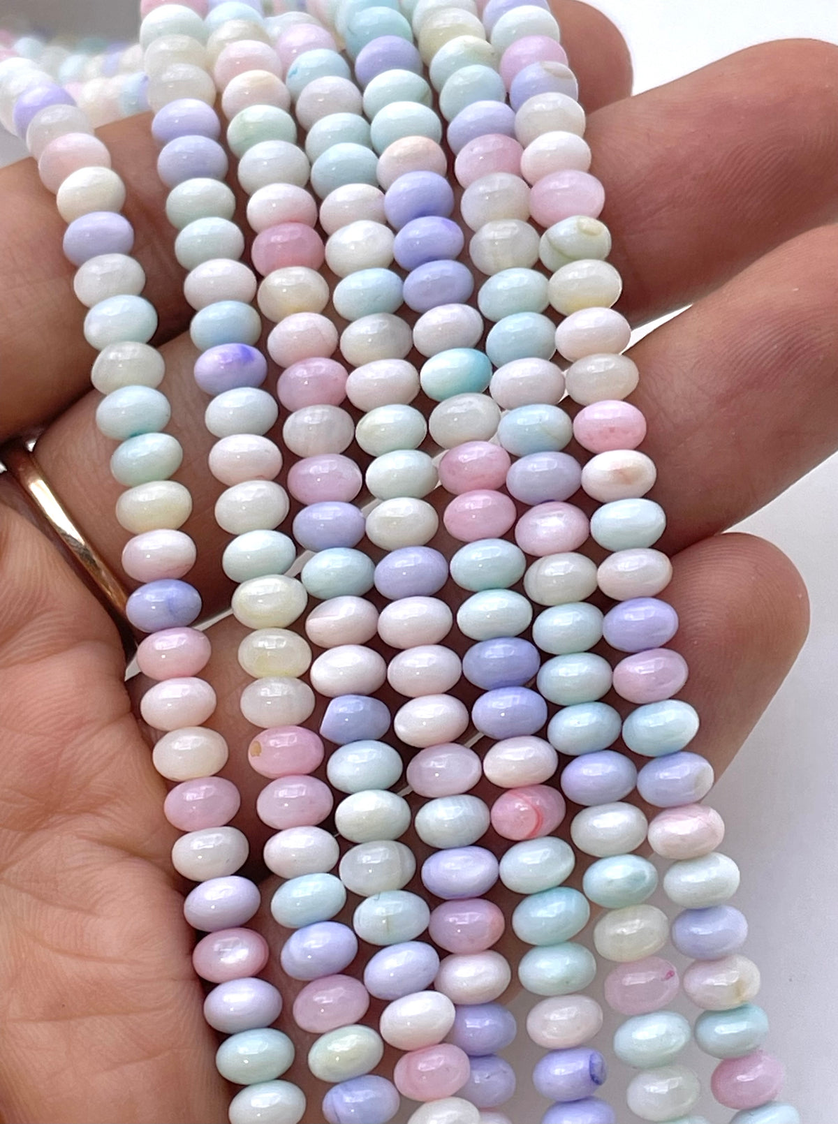 Multiple strands of small round pastel beads held in a hand. The beads have an iridescent, milky finish with soft pastel colors including pink, lavender, blue, and white.