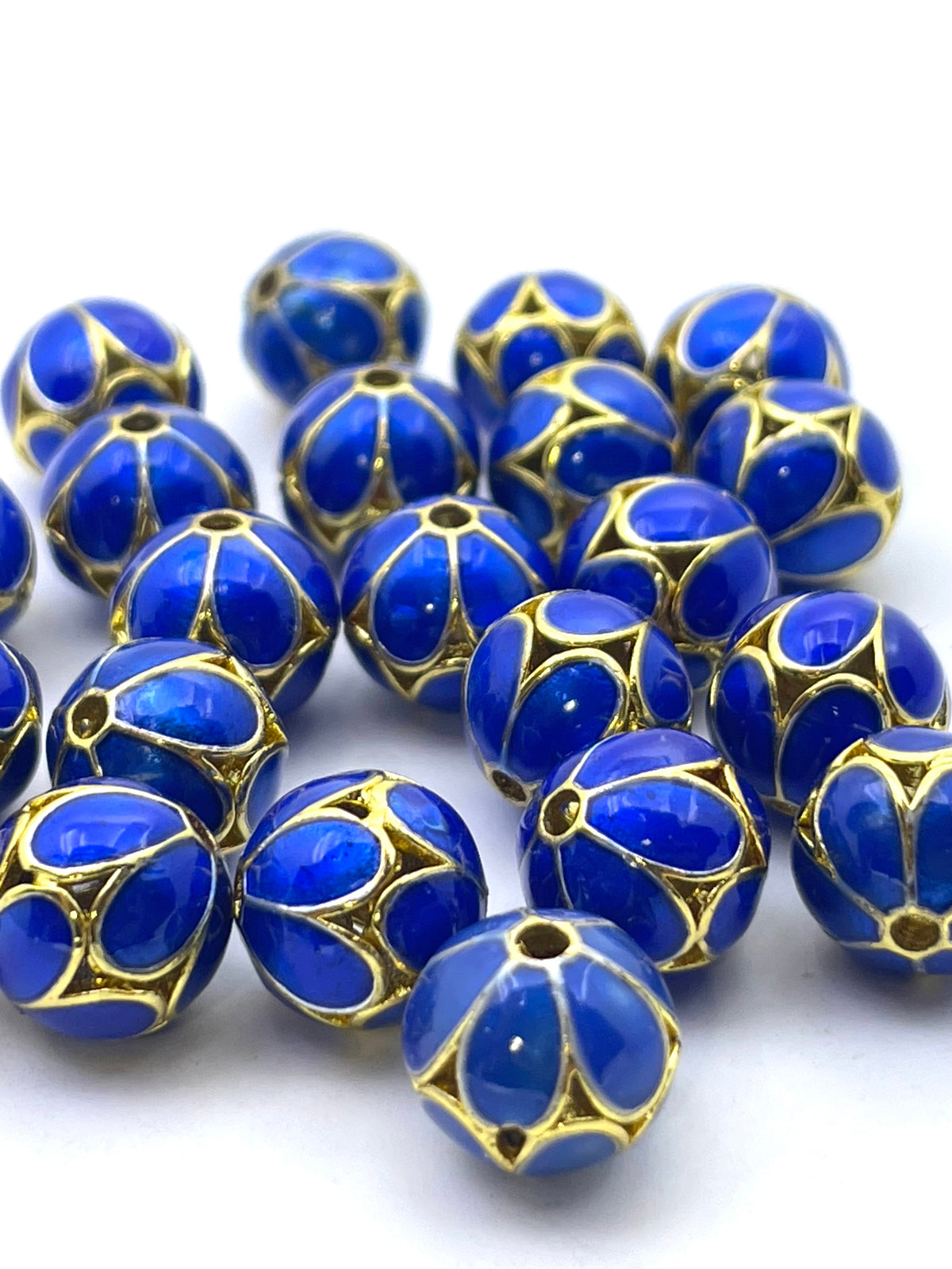 A pile of round blue glass beads with gold metal filigree cutouts, displayed on a clean white background.