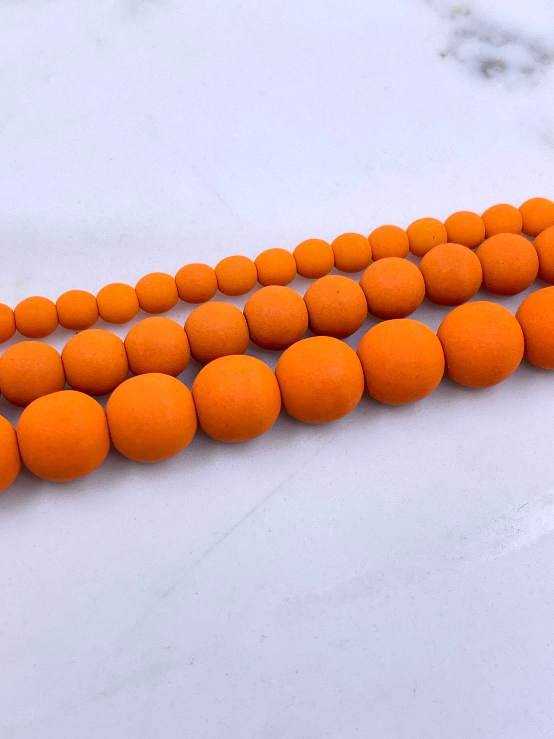 Orange matte spherical beads strung in two parallel rows on a light gray marble surface.