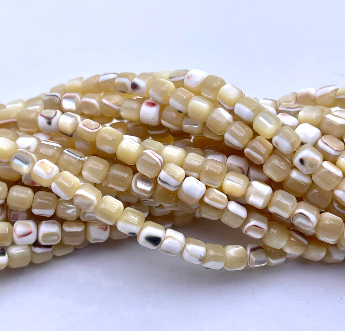 Close-up of multiple strands of small caramel mother of pearl square beads with a glossy finish, featuring a mix of cream, beige, white, and subtle black and red marbled patterns.