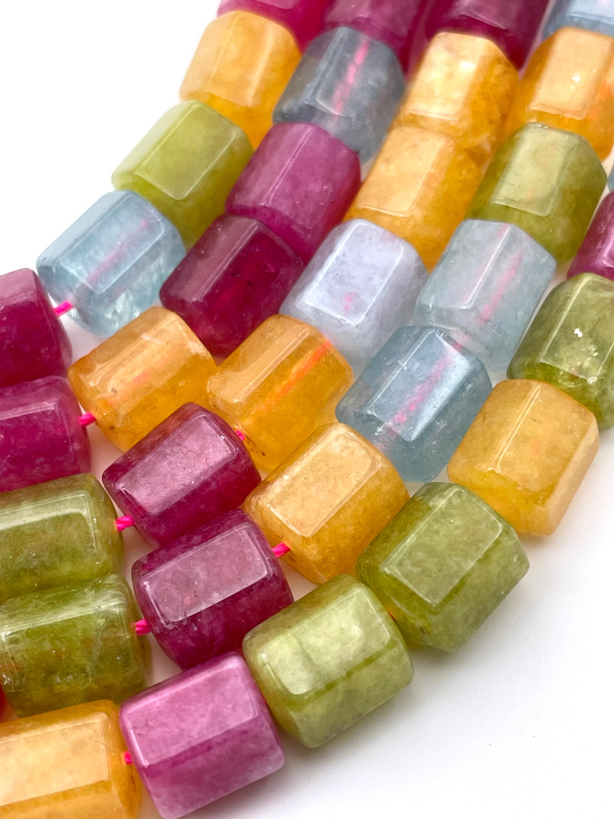 Close-up of faceted jade gemstone beads strung on pink cords, showing translucent colors including yellow, green, blue, and magenta on a white background.