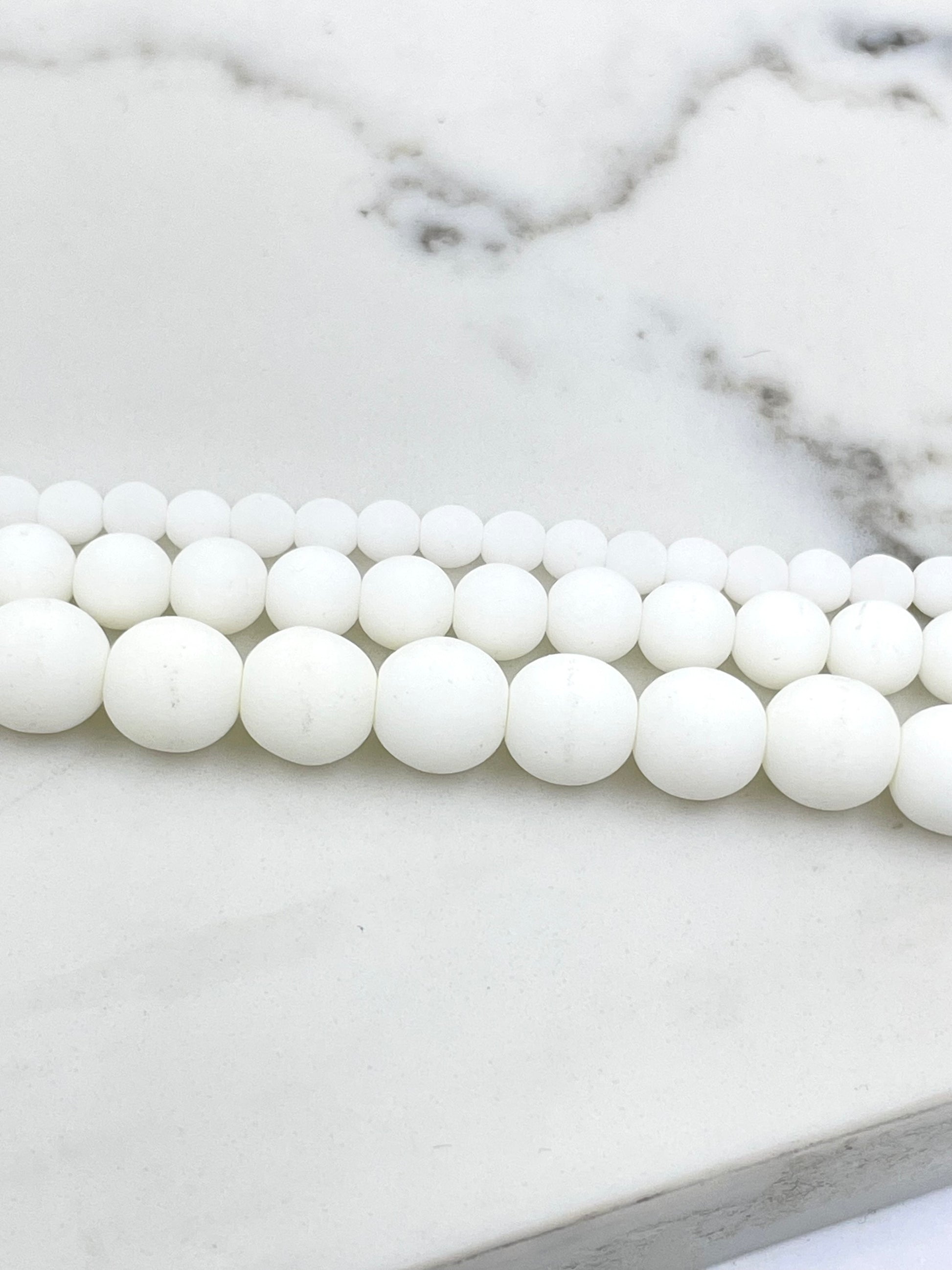 White round beads strung in three parallel rows on a white marble surface.