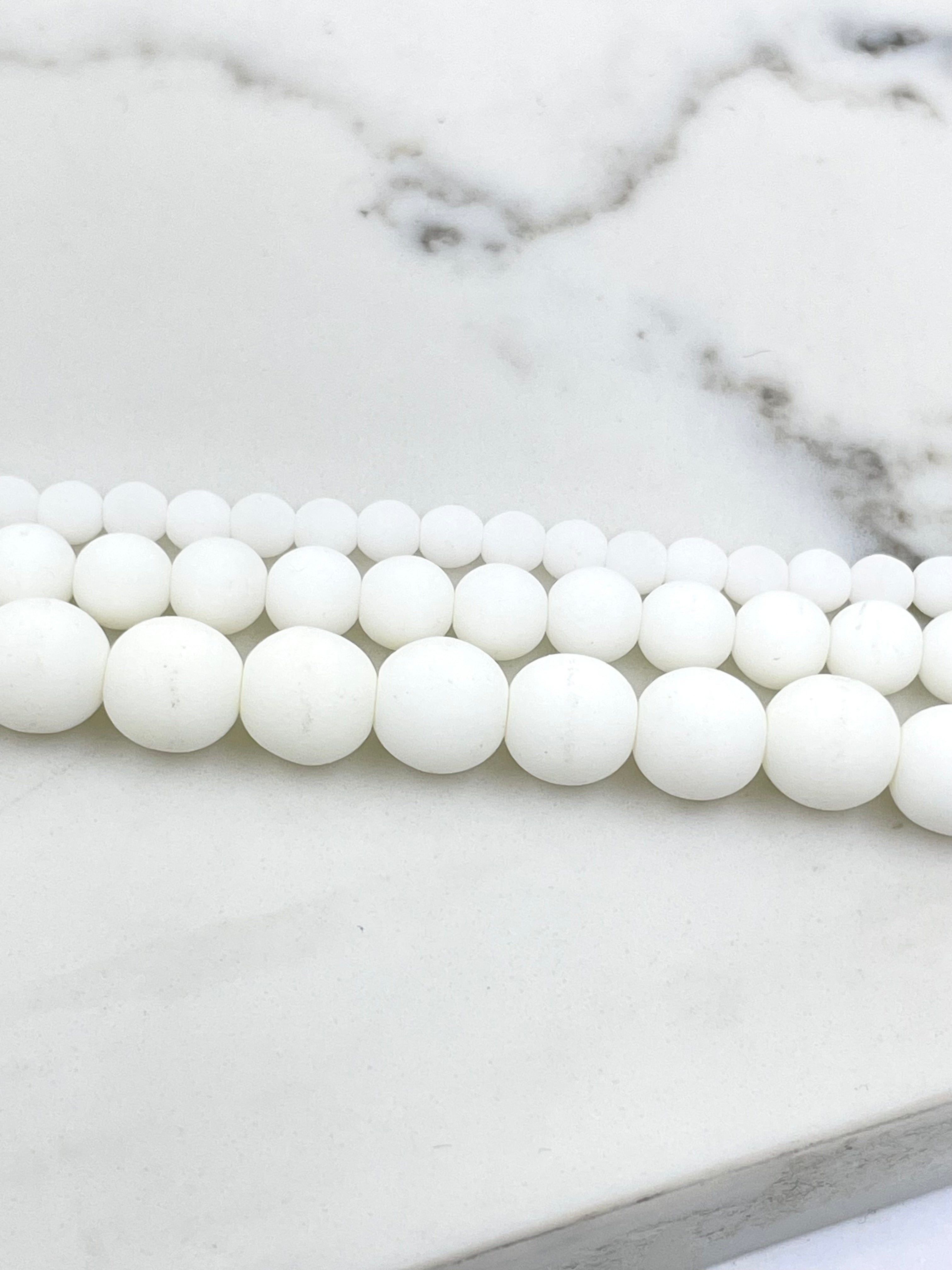 White round beads strung in three parallel rows on a white marble surface.