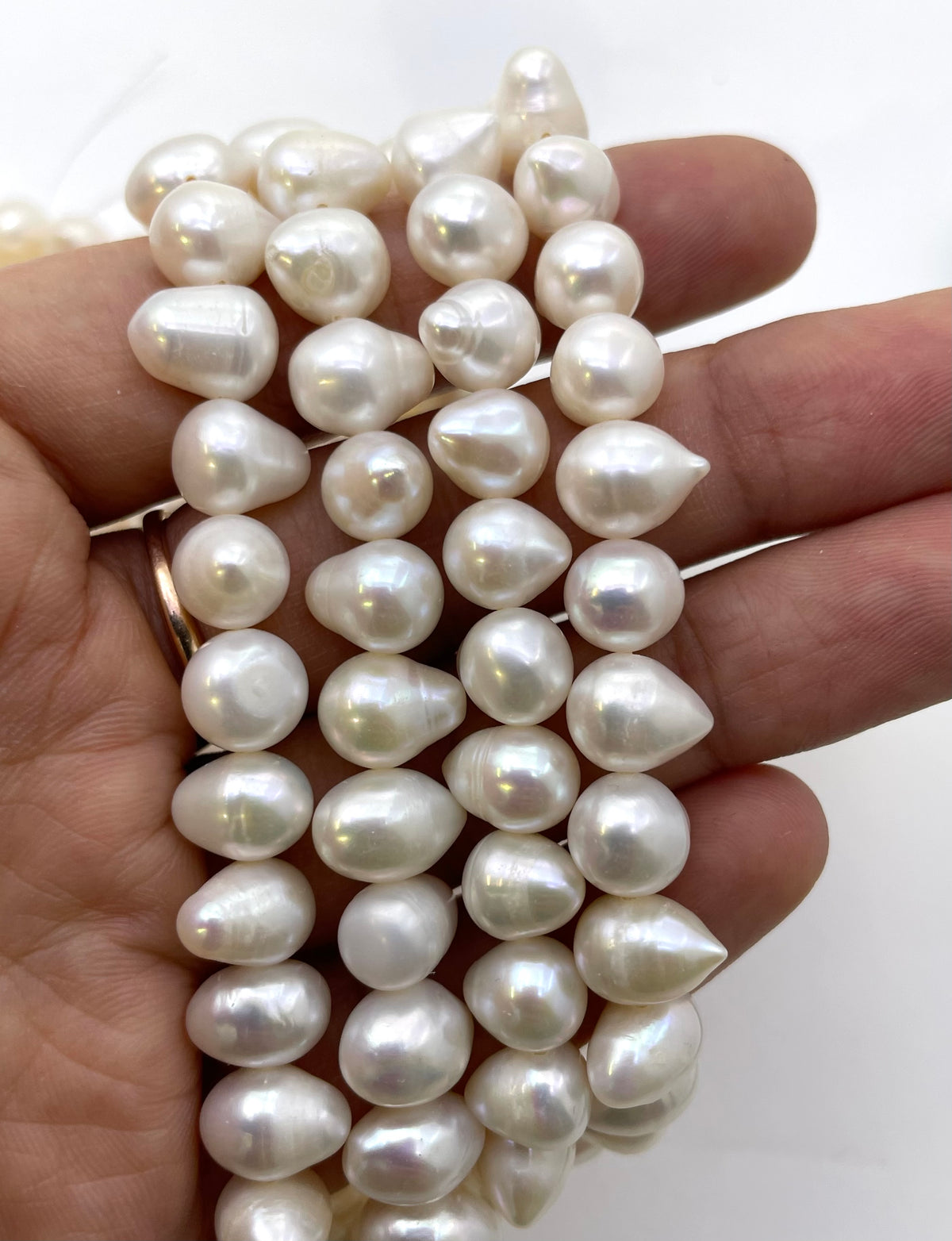 A close-up of a hand holding several strands of irregular white freshwater pearls, showing their lustrous, teardrop-like shapes against a plain white background.
