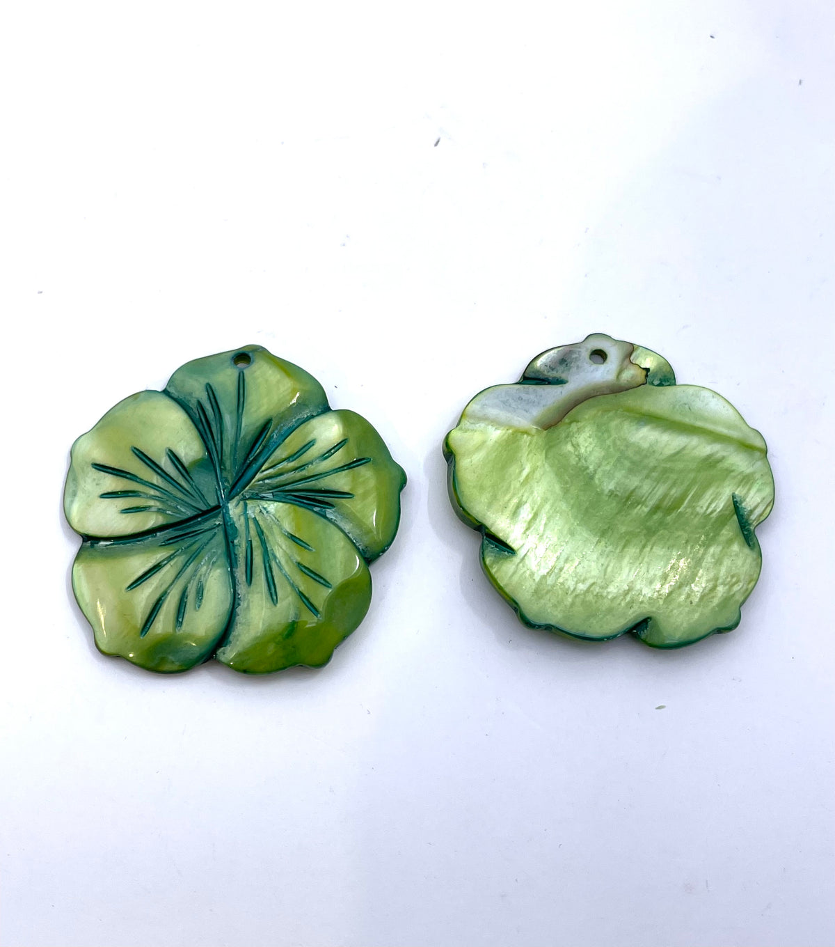 Two green mother-of-pearl flower-shaped pendants, one showing the front with dark green petal lines and the other showing the back on a plain white background.