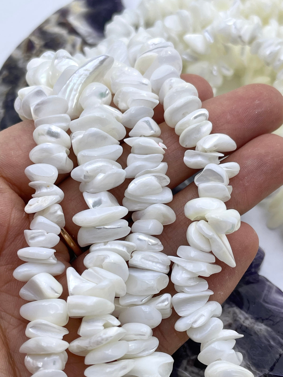 White irregular shell beads draped over a hand, with strands of matching beads blurred in the background.