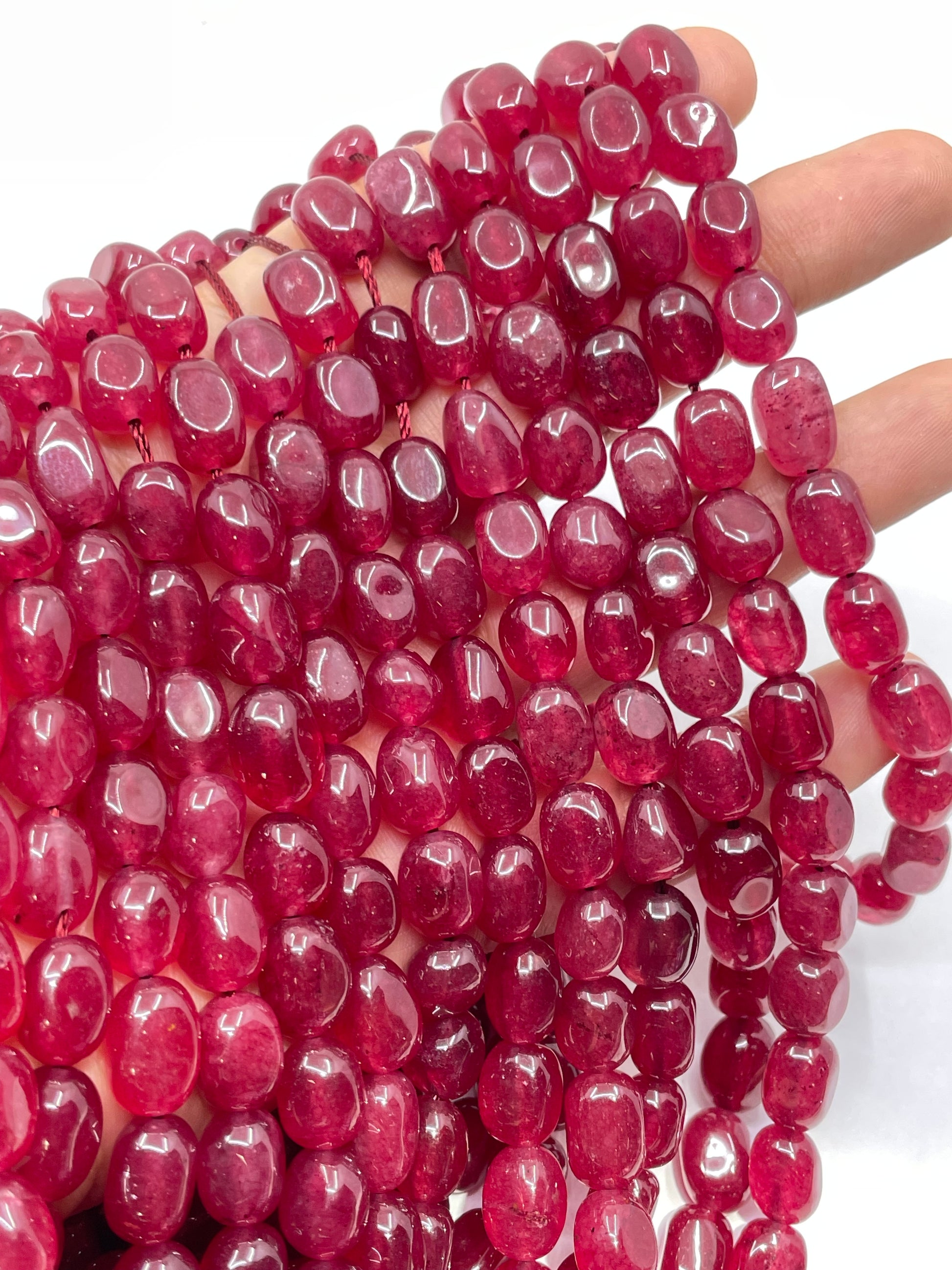 A close-up of a hand holding multiple strands of polished, faceted dark pinkish-red jade beads against a plain white background.