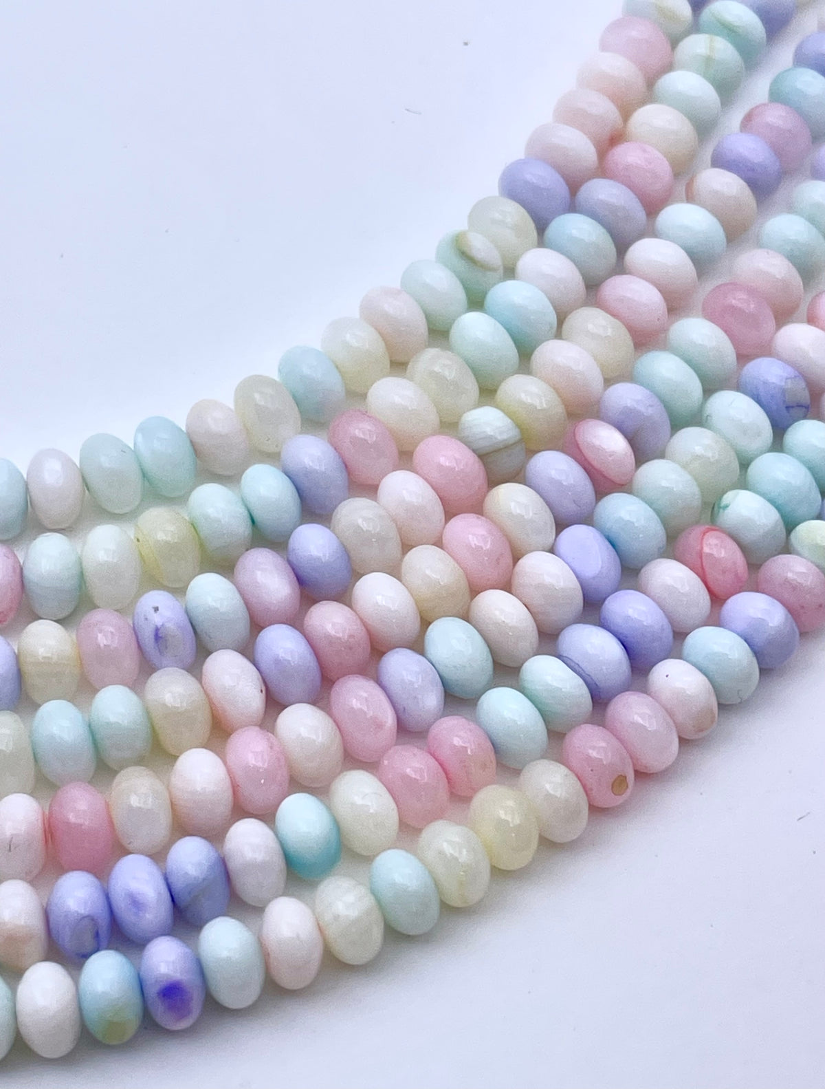 Multiple strands of small oval beads in pastel rainbow colors, including pink, blue, purple, green, and yellow, arranged diagonally on a plain white background.