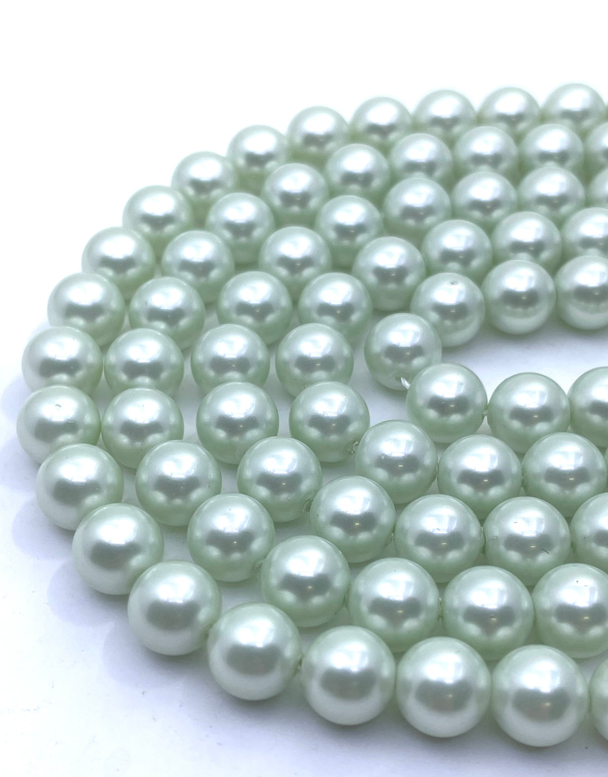A close-up of multiple strands of round shell pearl beads in a pale mint green color, arranged on a plain white background.