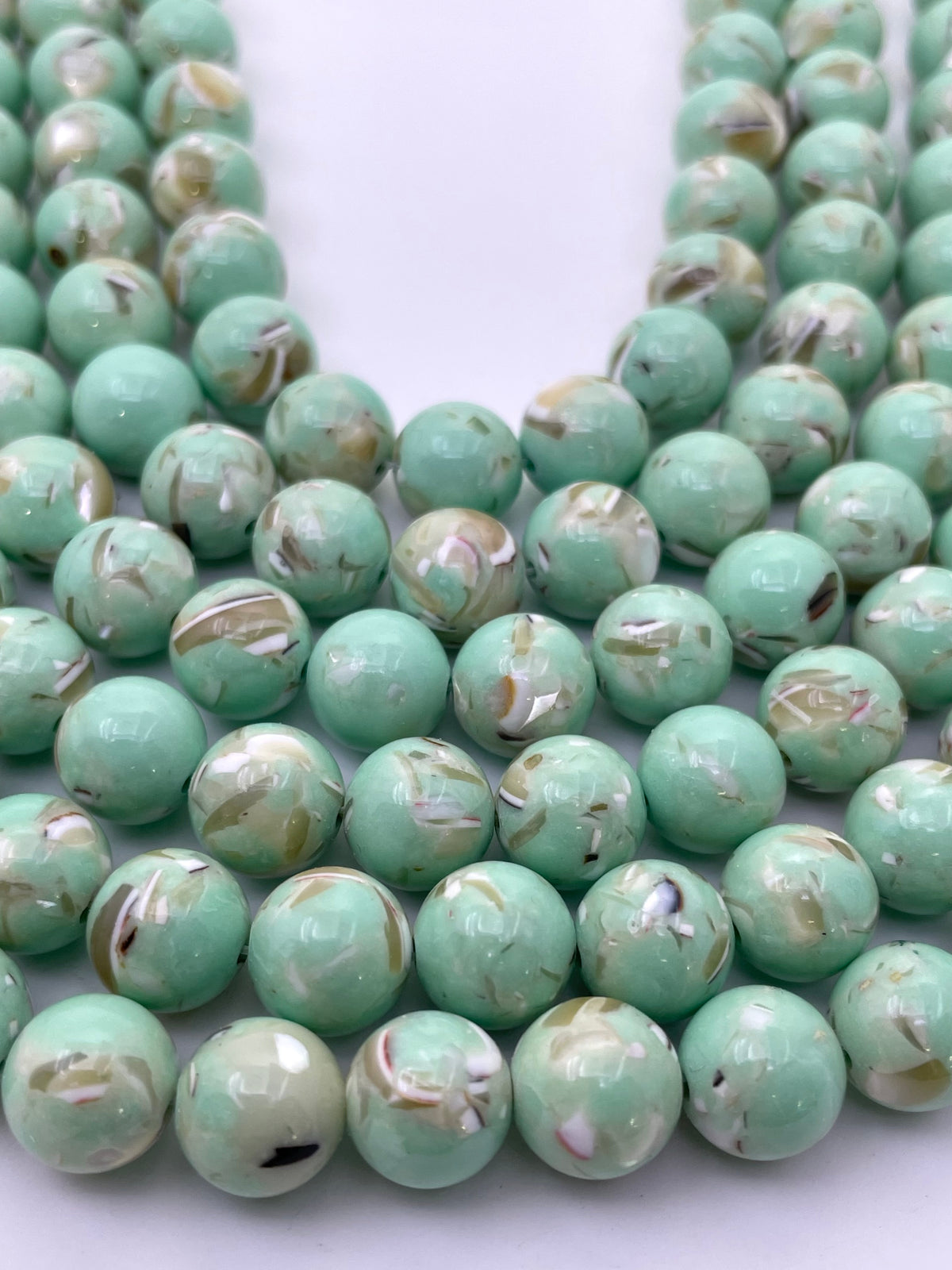 Green marbled mop beads with white and brown swirls, arranged in strands on a white background.