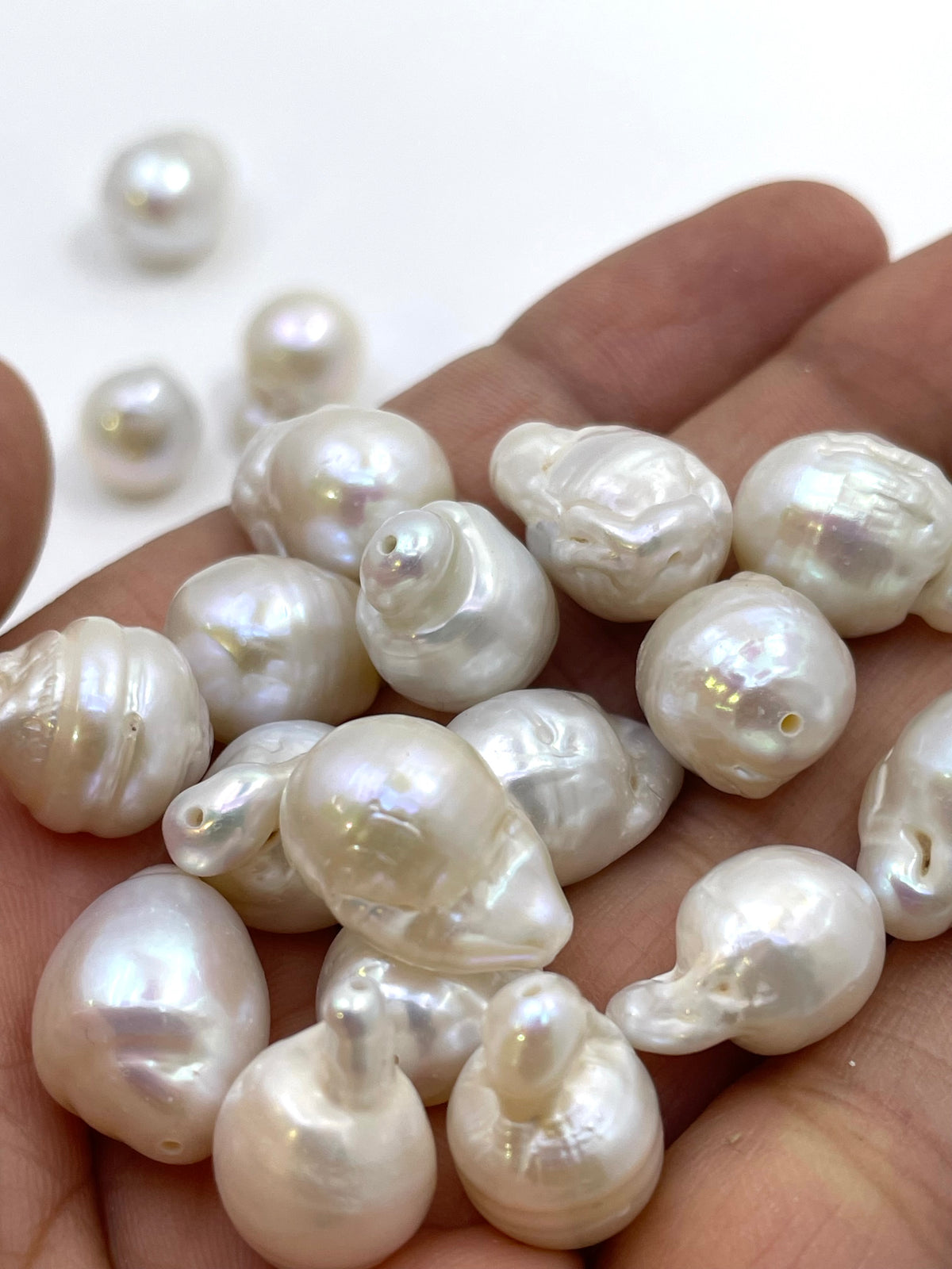 Barrel-shaped freshwater pearl beads in an off-white lustrous finish, held in a person's palm with a few more beads scattered in the background.