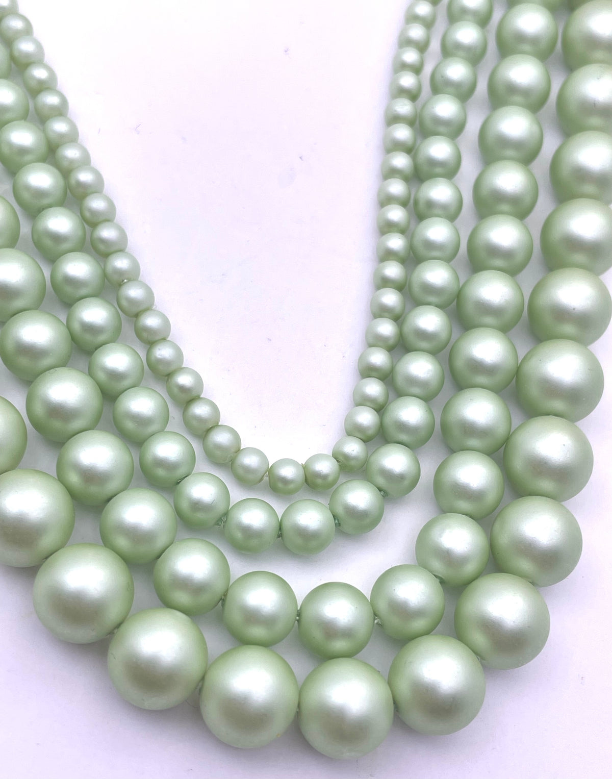 Multiple strands of light green shell pearl beads in various sizes, arranged in a layered display on a plain white background.