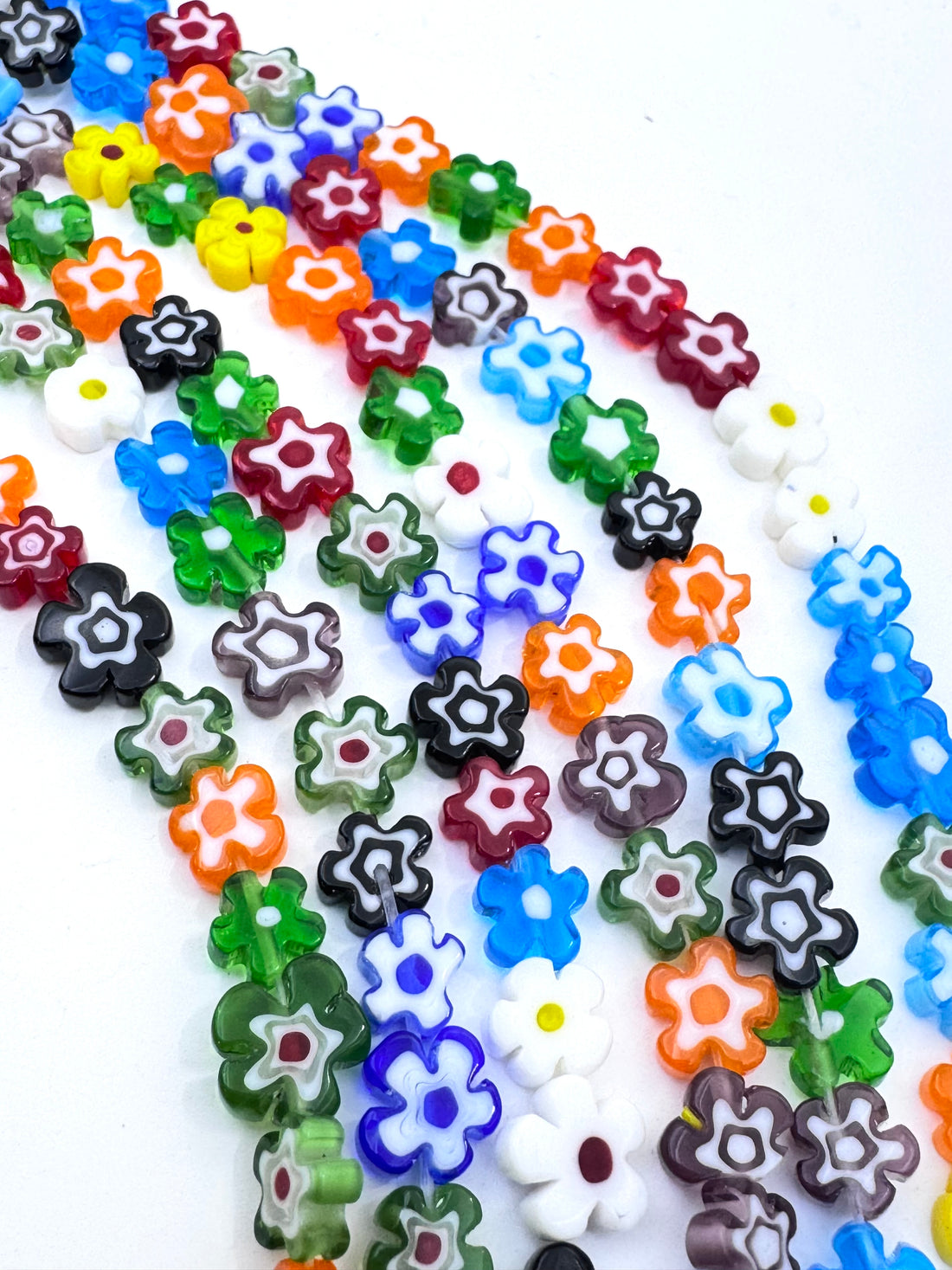 A hand holding several strands of colorful flower-shaped beads on a white background.