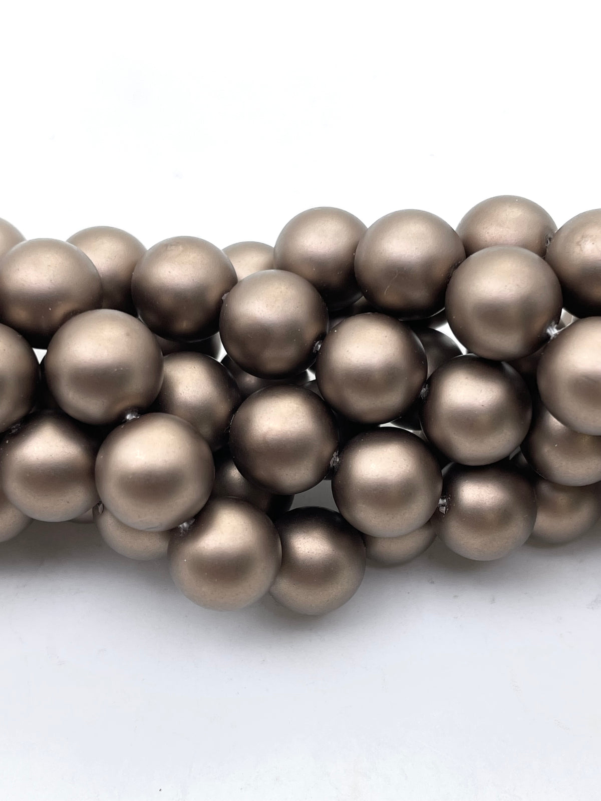 A close-up of a strand of Pearlescent Chocolate Brown round shell pearls on a plain white background.