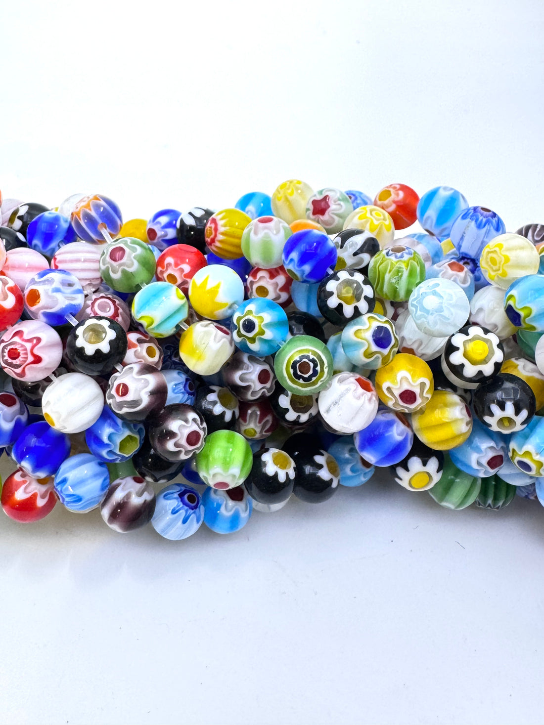 A close-up of a multi-strands of colorful glass beads with various patterns including floral, striped, and solid colors on a white background.