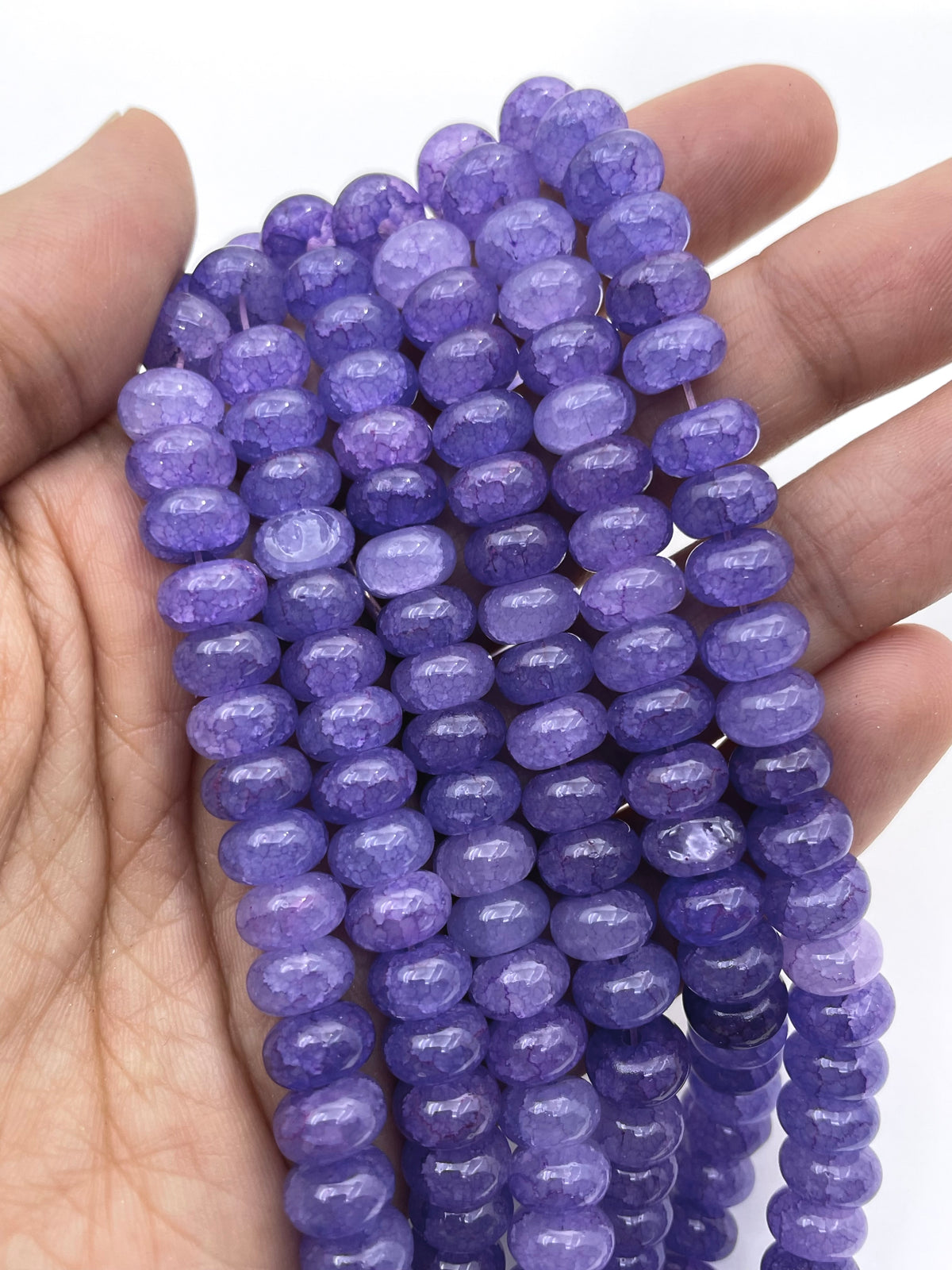 Purple glass beads draped over a hand against a white background.