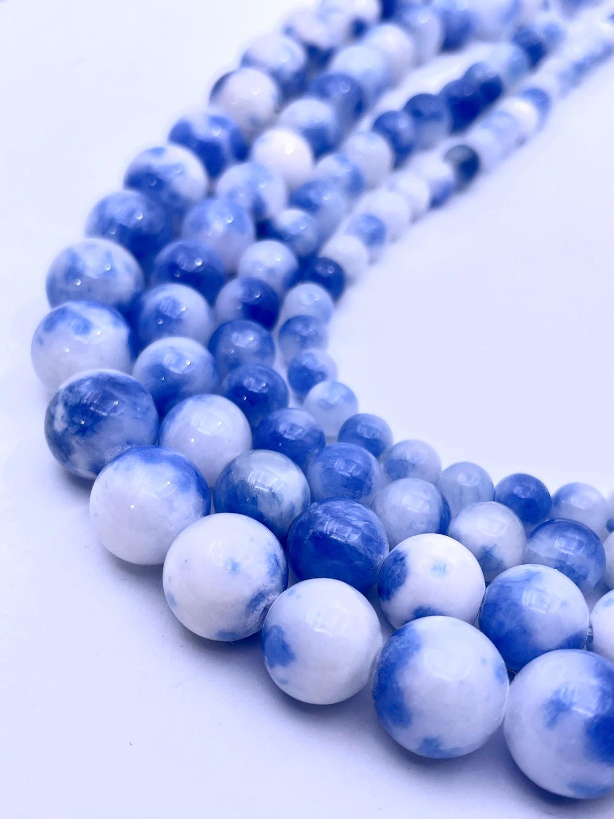 Blue and white marbled round perisan jade gemstone beads arranged in a curved row on a plain white background.