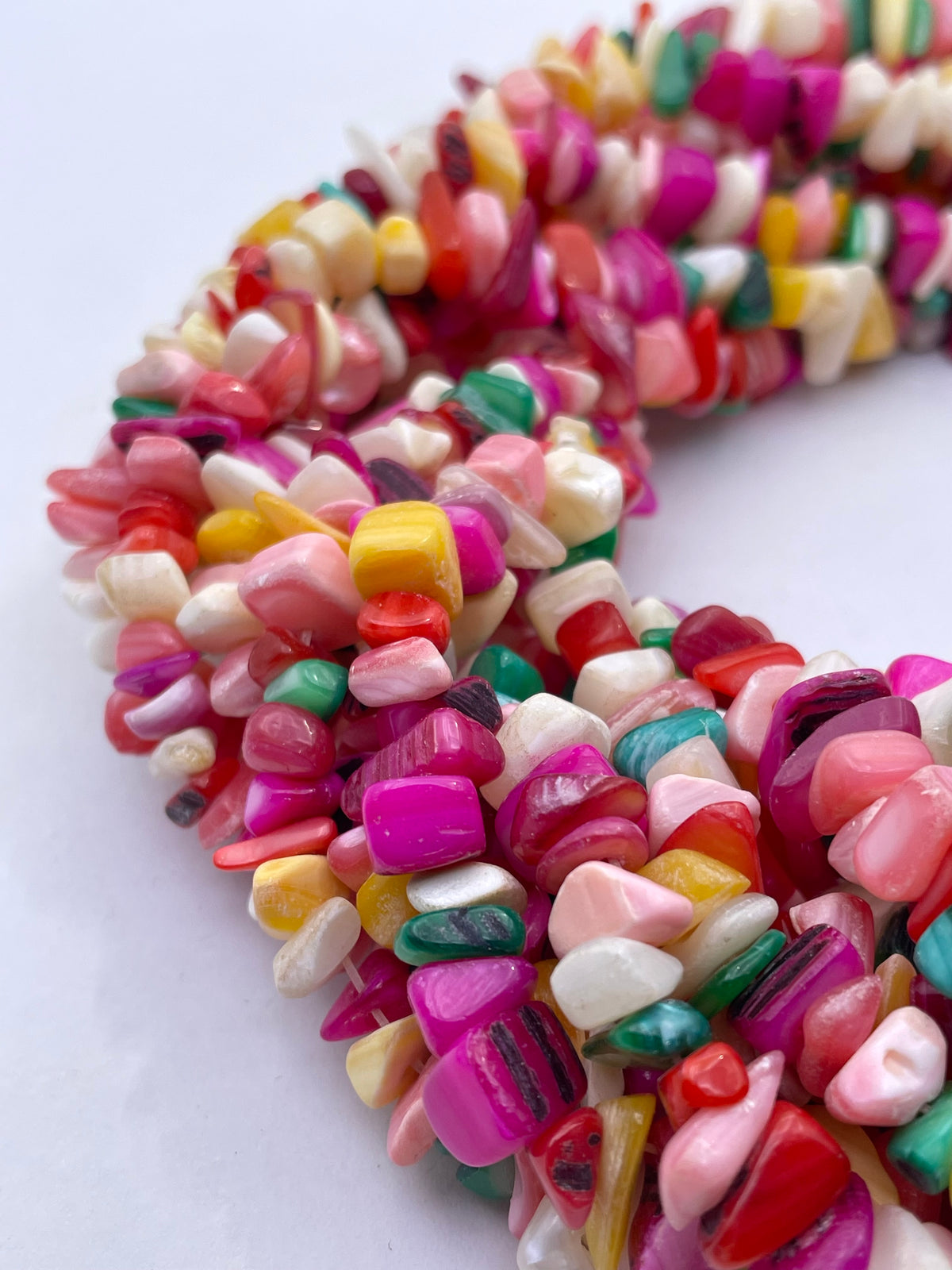 A close-up of a curved strand of colorful tumbled mop stone beads on a plain white background.