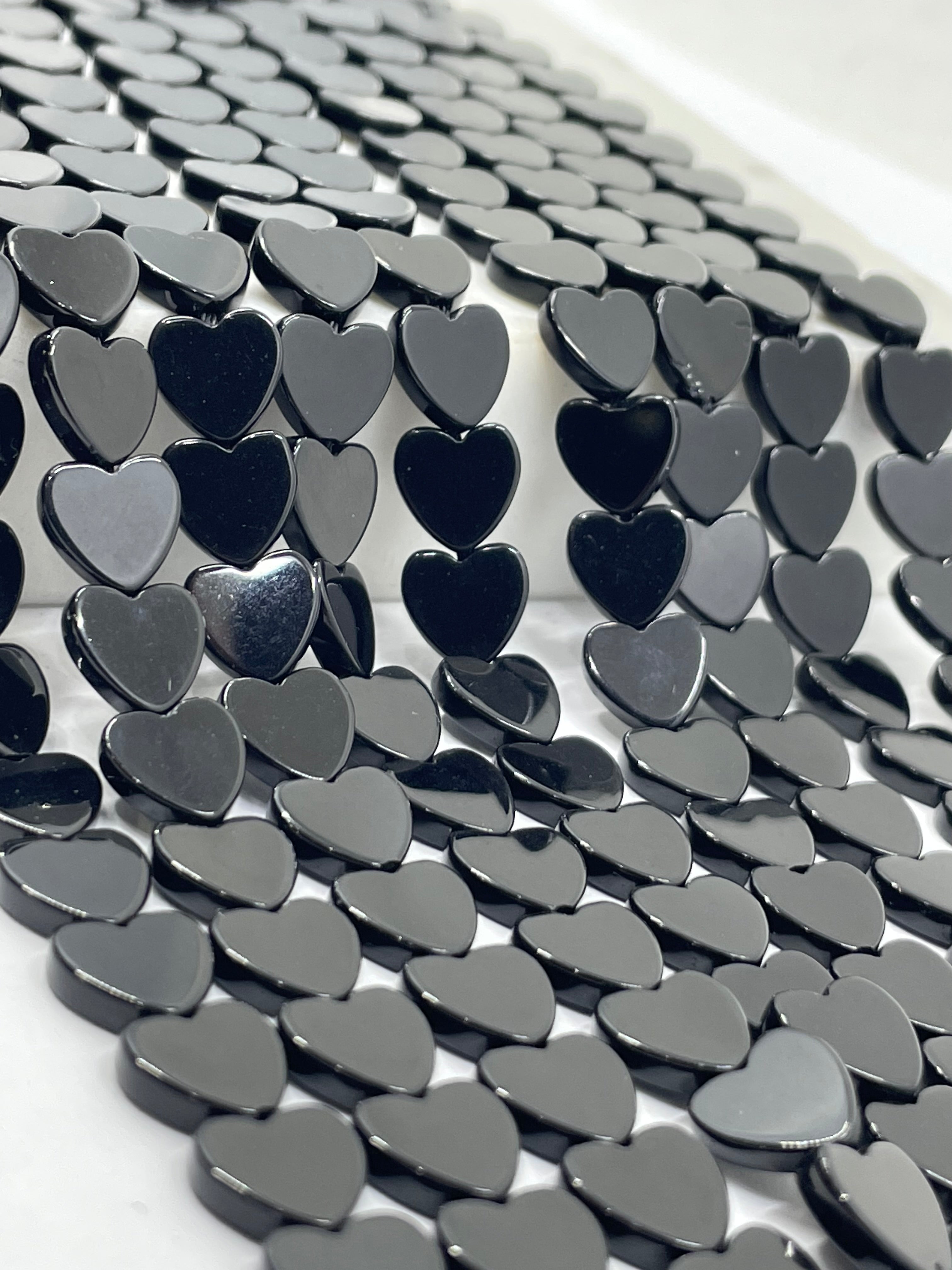 A close-up of many glossy black agate heart-shaped pieces arranged in a repeating pattern against a white background.
