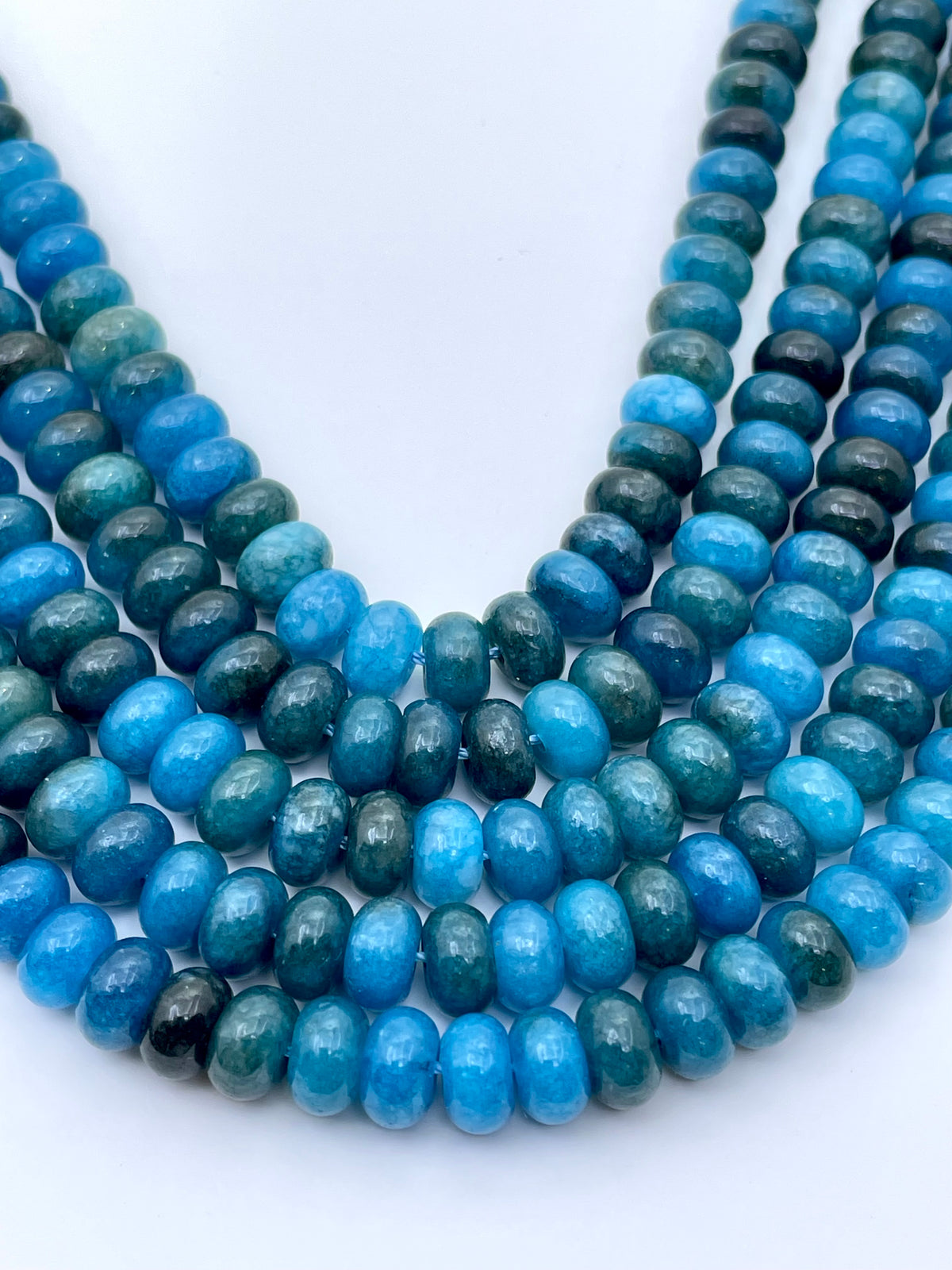 Smooth donut apatite jade beads curved strands against plain white background
