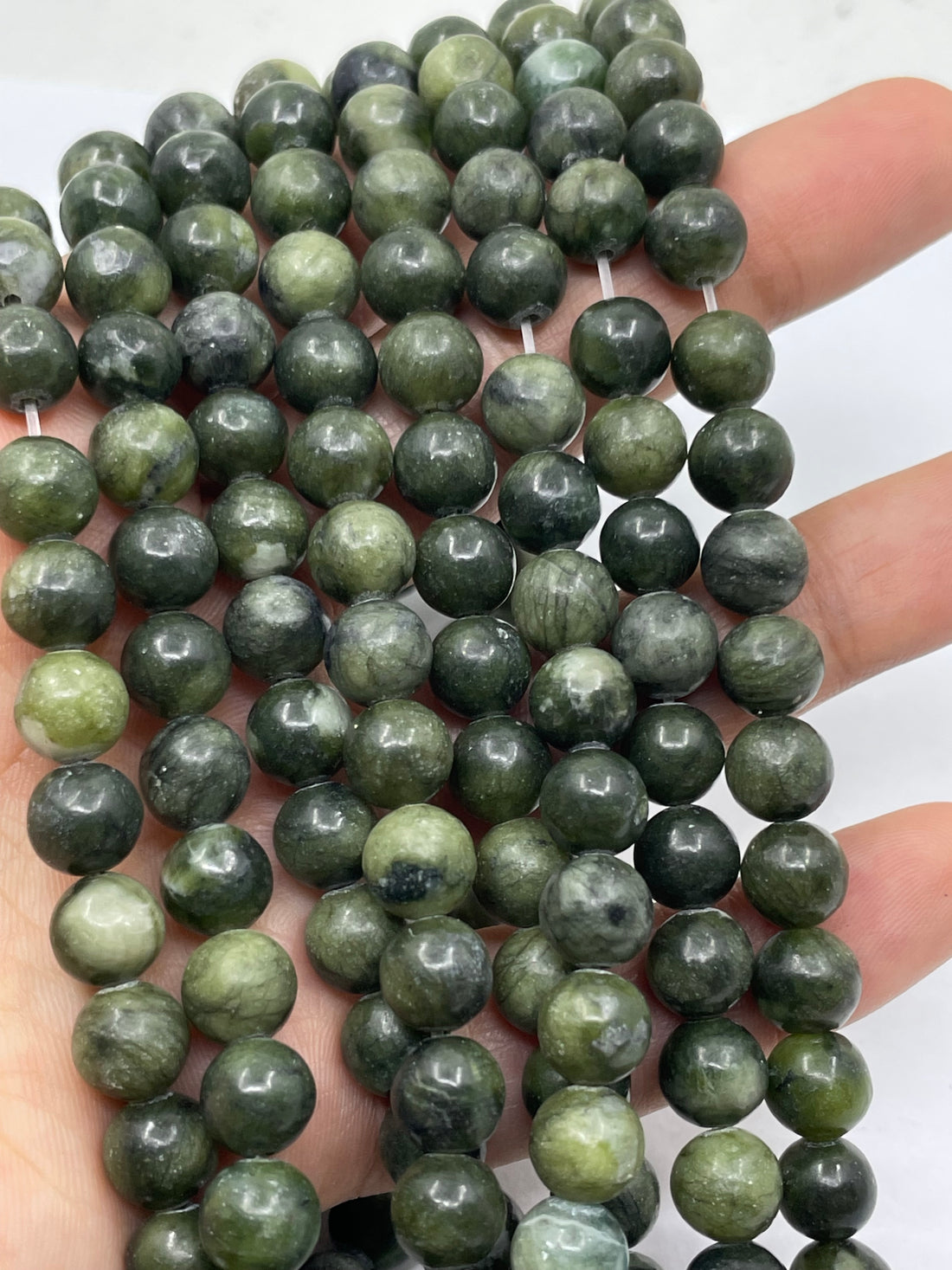 Multiple strands of round green jade stone beads arranged in curved rows on a plain white background.