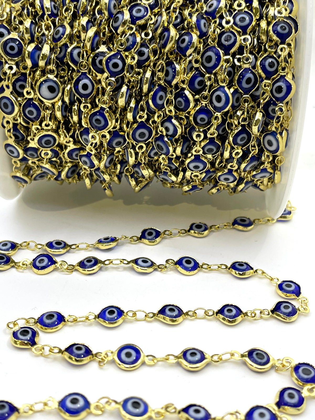 Gold chain with blue evil eye, shown spool-wrapped and draped on a white surface.