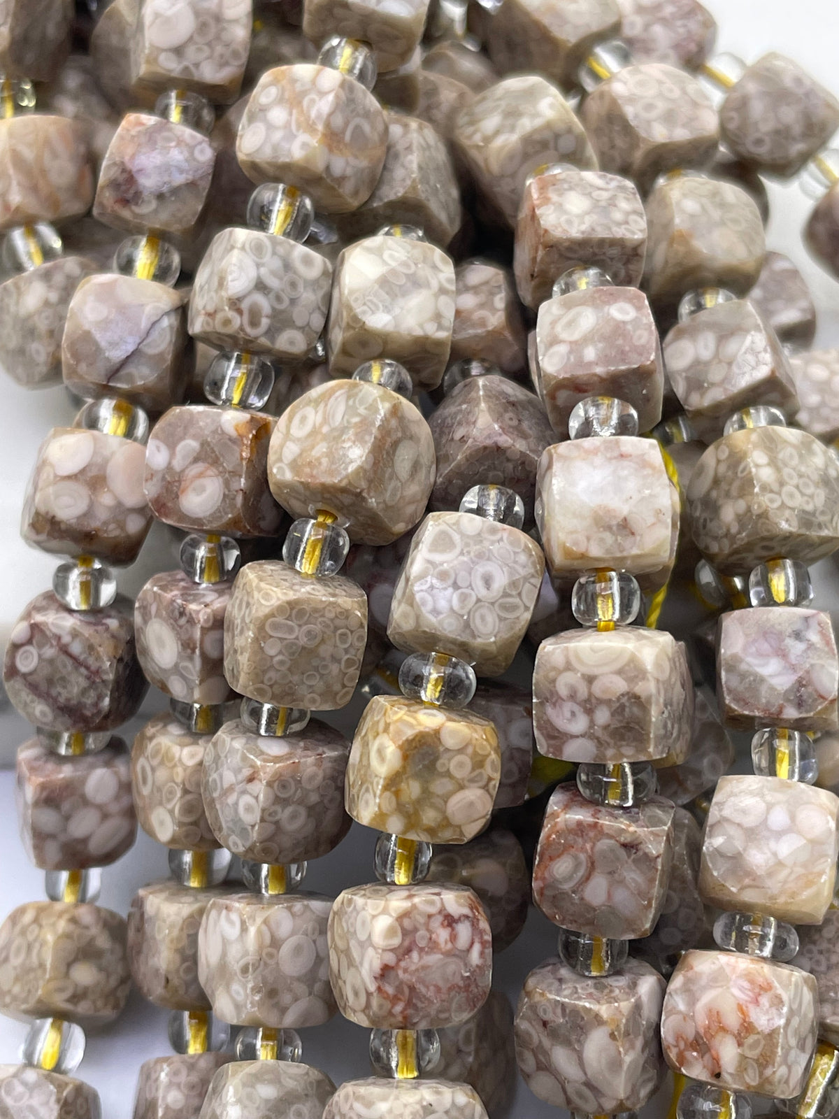 Close-up of faceted stone cube beads strung on clear cords, showing a mottled pattern in beige, brown, and white with small clear spacer beads.