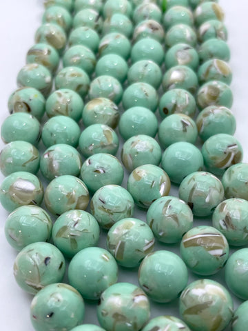 A close-up of multiple strands of round, glossy mop beads in a light mint green color with natural marbled swirls of white, beige, and brown.
