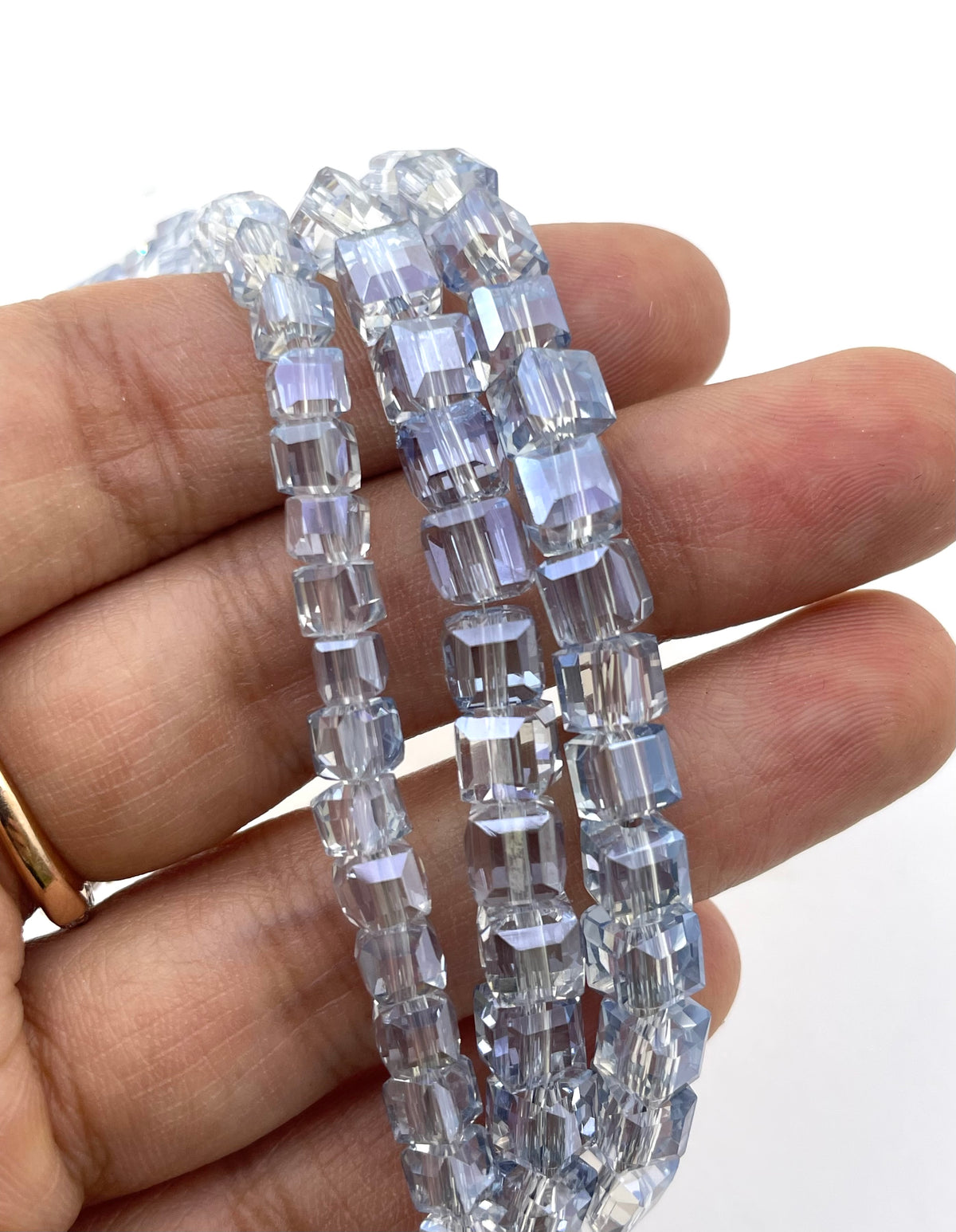 Three strands of faceted monatana blue beads held in a hand, showing their transparent and reflective properties against a white background.