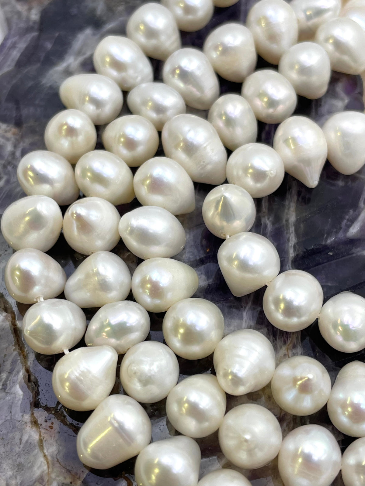Close-up of irregular white freshwater pearl beads arranged on a dark marbled surface.