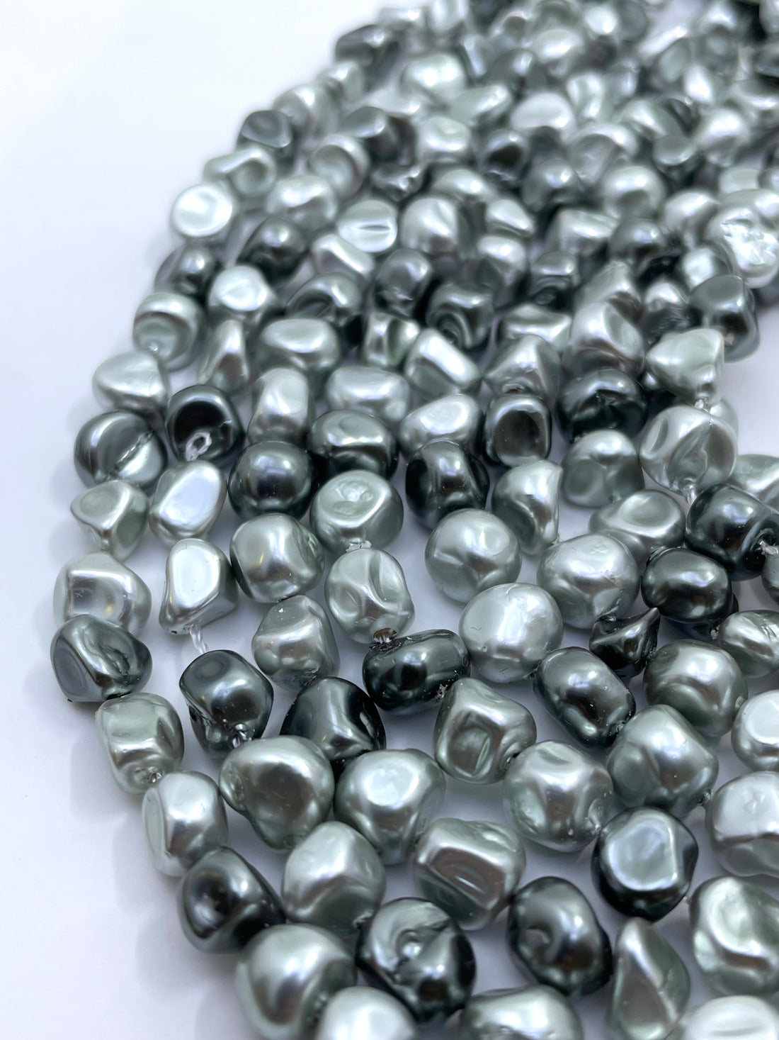 Close-up of a strand of irregular, metallic silver or grey shell pearl beads on a plain white background.