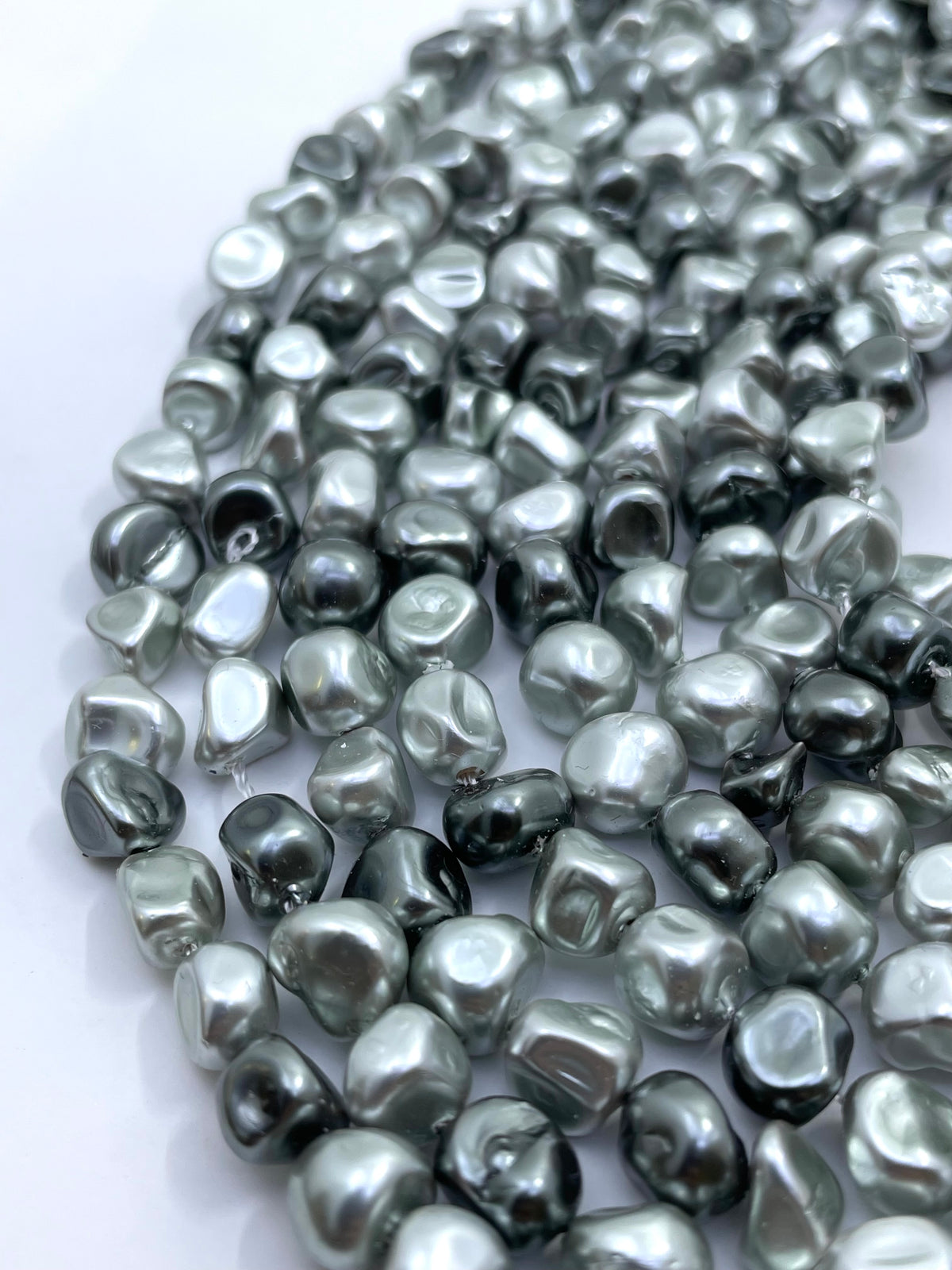 Curled strands of irregular shell pearls in a metallic silver-gray color, arranged on a plain white background.