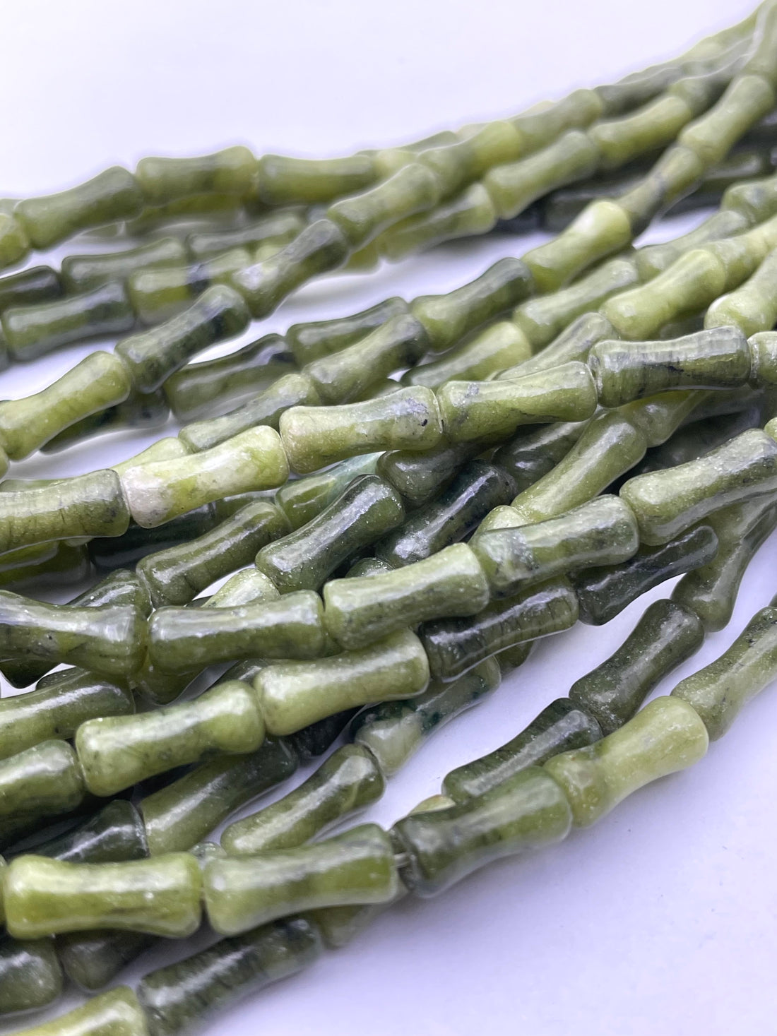 Green nephrite jade stone beads with a natural marbled texture, arranged diagonally on a plain white background.