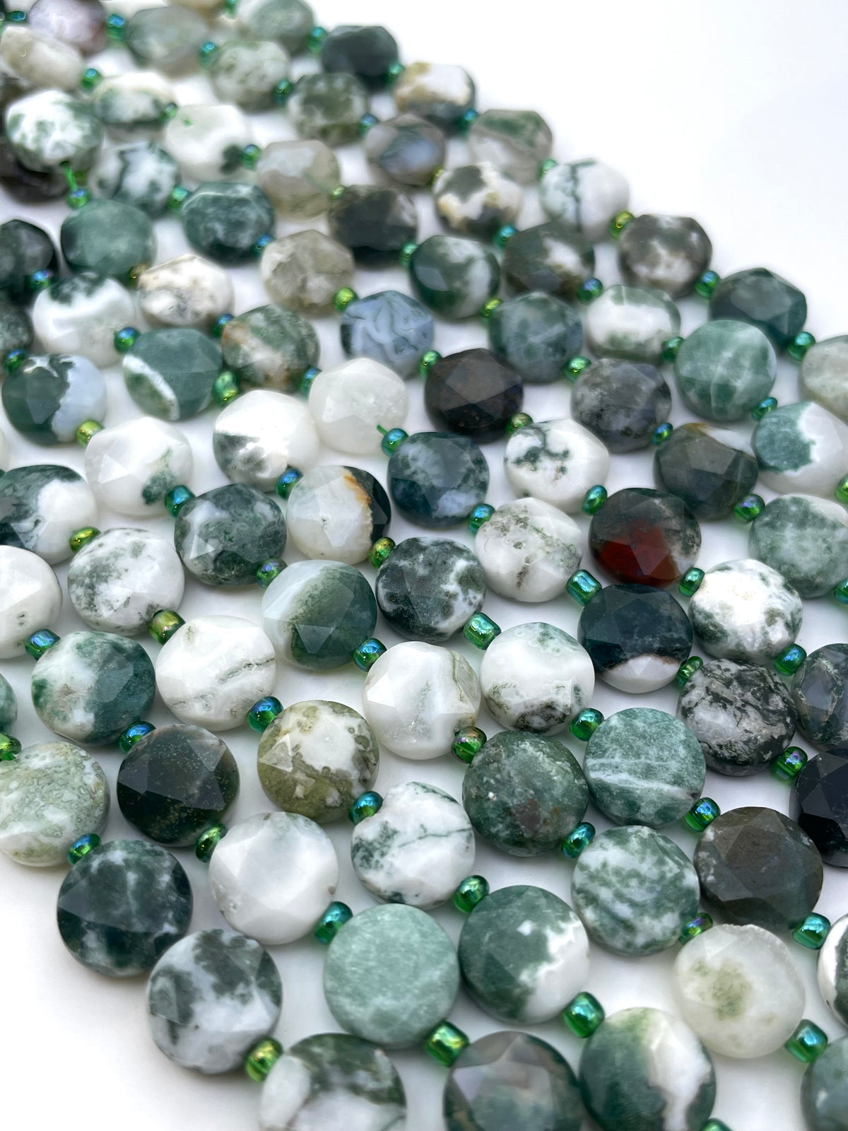 Faceted round tree agate gemstone beads in green, white, gray, and black marbled patterns, strung with small metallic green spacer beads on a white background.