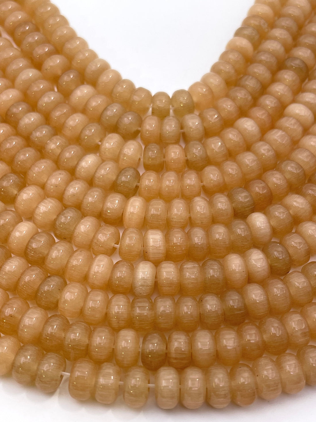 A close-up of multiple strands of smooth, round, translucent cats eye beads held in a person's hand against a plain white background.