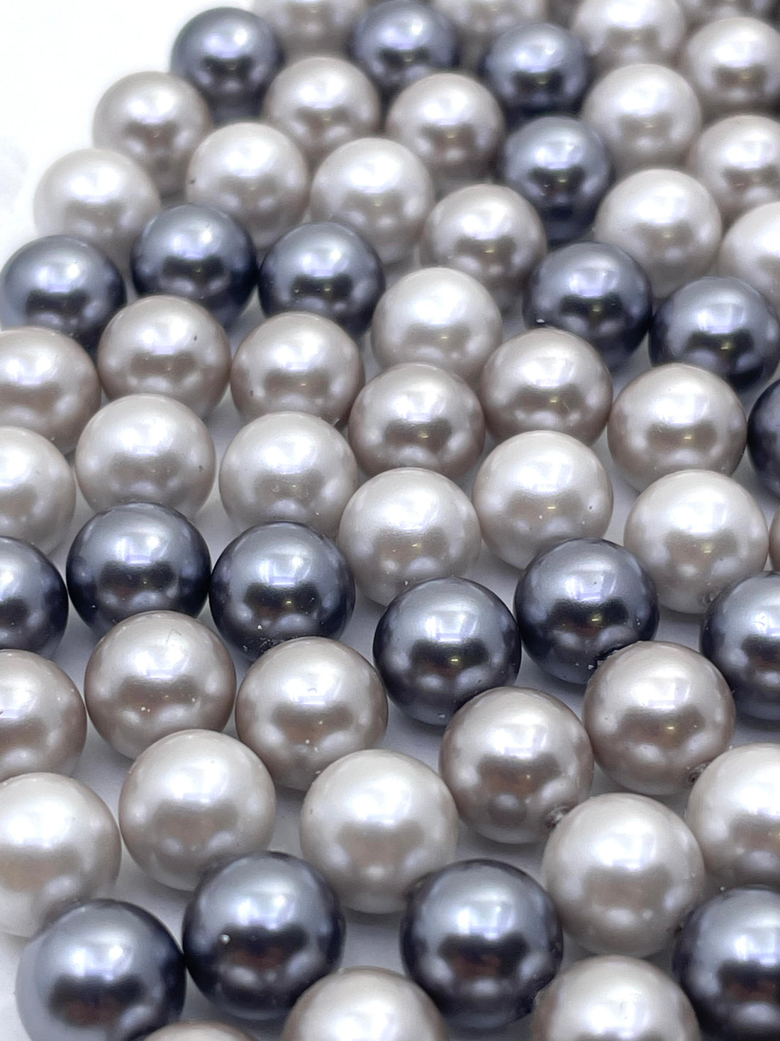 A close-up of shell pearl beads in mixed colors, including cream, light gray, charcoal, and dark navy, arranged in overlapping rows.