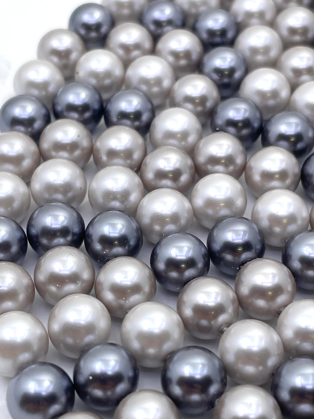 A close-up of shell pearl beads in mixed colors, including cream, light gray, charcoal, and dark navy, arranged in overlapping rows.