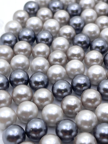 A close-up of shell pearl beads in mixed colors, including cream, light gray, charcoal, and dark navy, arranged in overlapping rows.