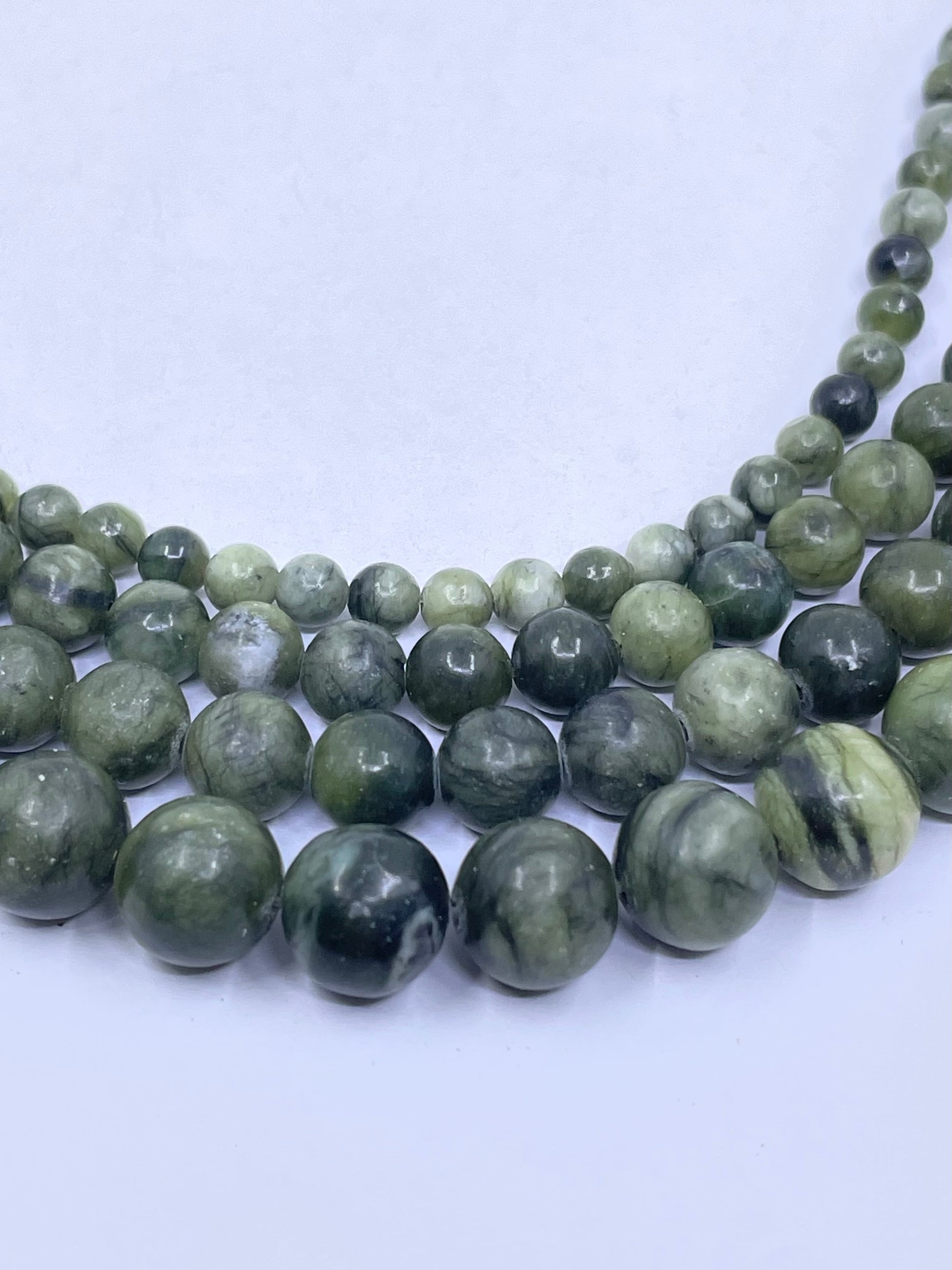 Three strands of polished round jade gemstone beads in shades of green, gray, and black, arranged in a curve on a light gray background showing sizes.