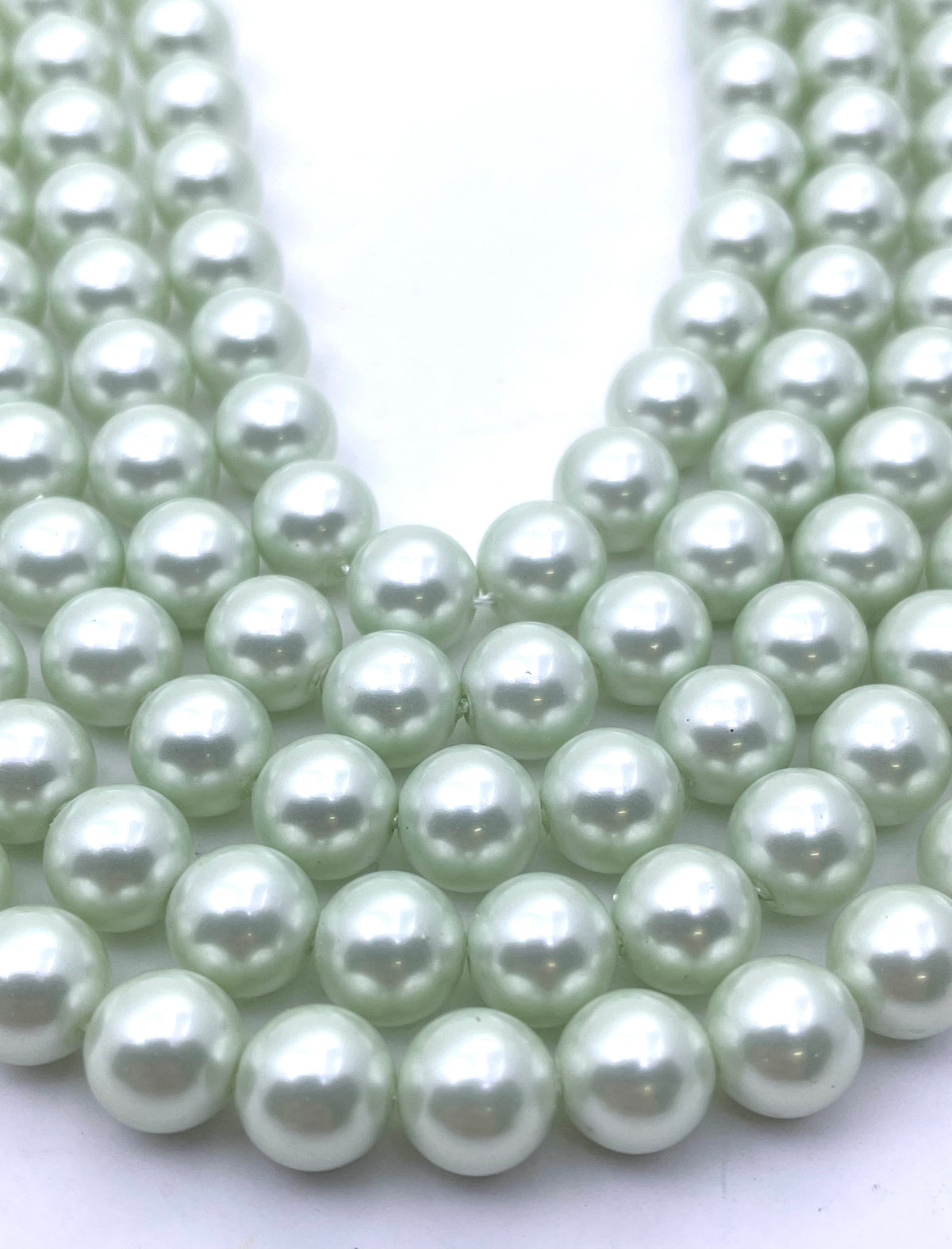 Multiple strands of round, lustrous shell pearl beads in a pale mint green color, arranged in a U-shape on a plain white background.