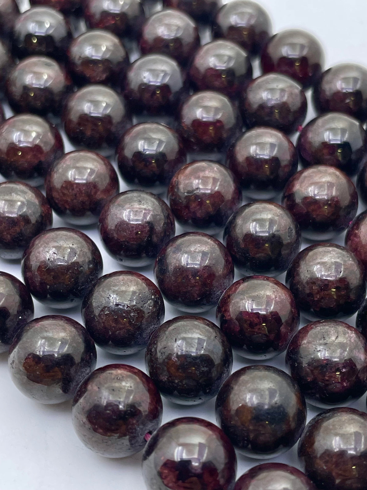 A close-up of glossy dark brown to black round garnet beads with subtle reddish-brown marbling, arranged in overlapping rows on a light background.
