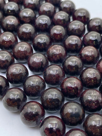 A close-up of glossy dark brown to black round garnet beads with subtle reddish-brown marbling, arranged in overlapping rows on a light background.