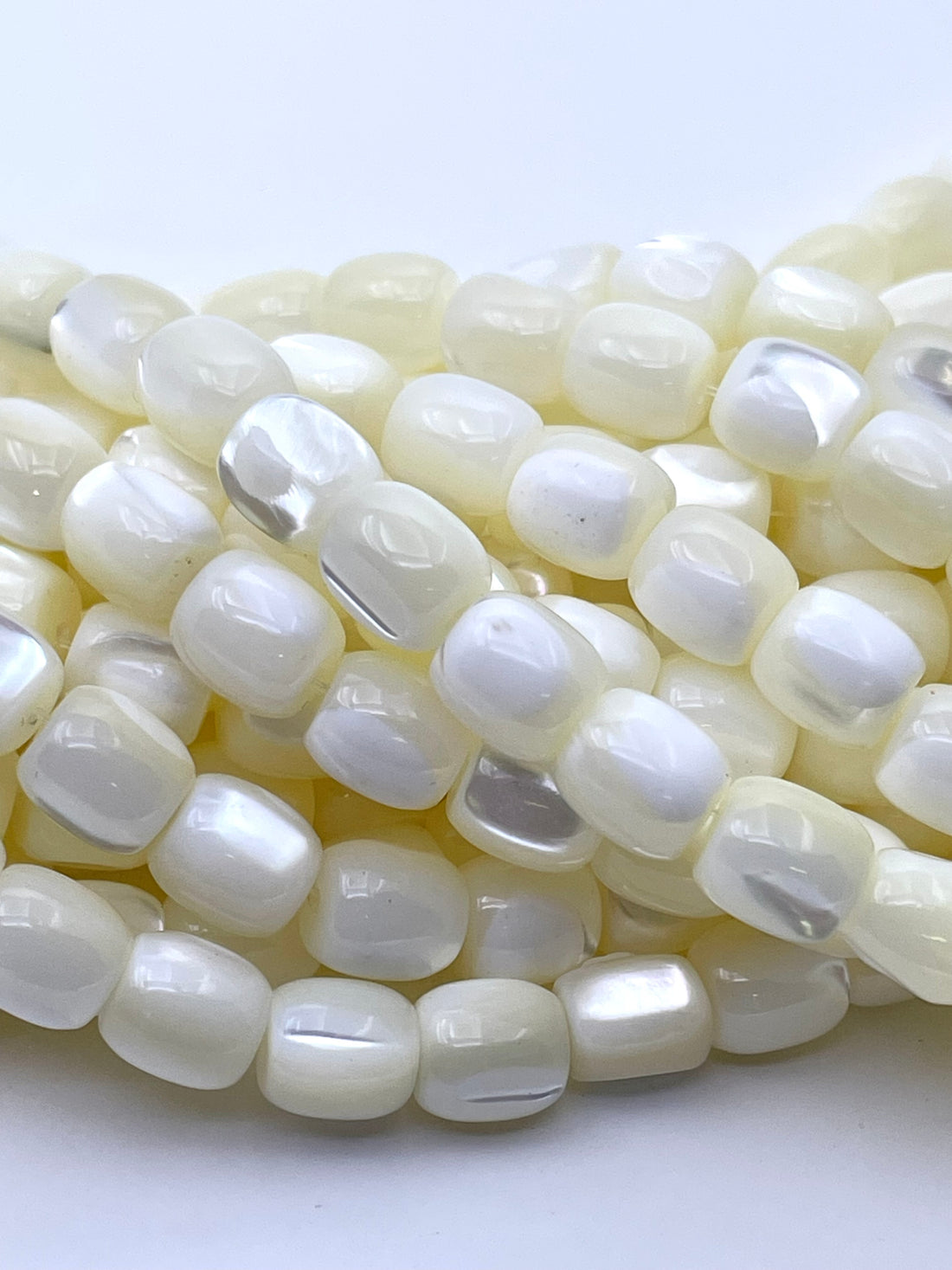A close-up of glossy, rounded rectangular beads with a pearlescent white and soft cream color, arranged in overlapping coils on a plain white background.
