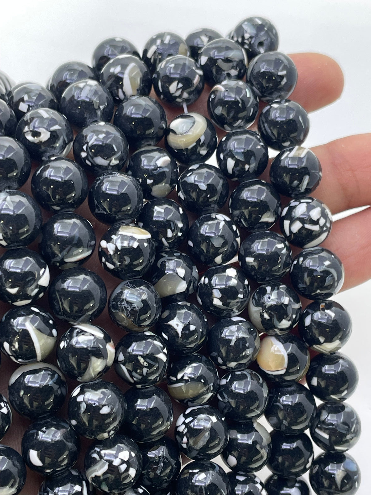 A close-up of glossy black mop beads with white marbled or swirled patterns, held in a hand against a plain light background.