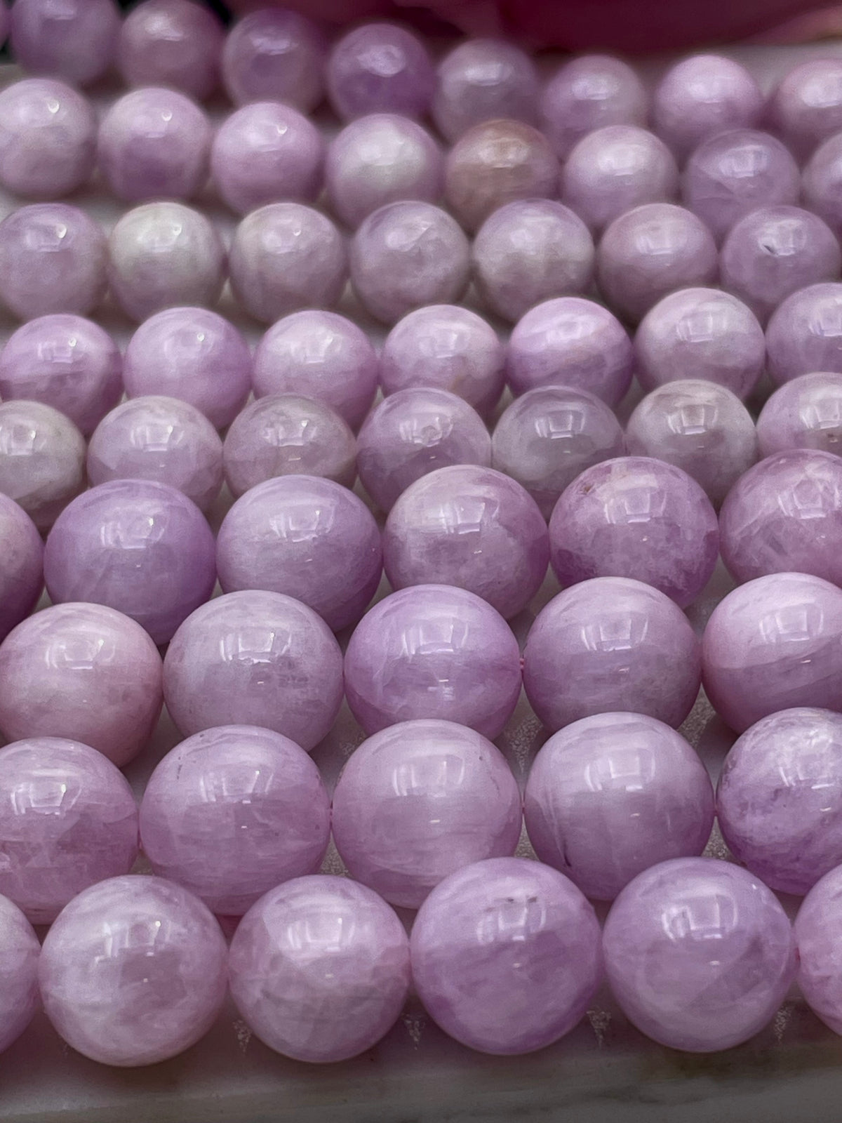 Rows of polished round lavender kunzite purple beads, likely from a raw crystal bead strand, arranged closely together on a light surface.