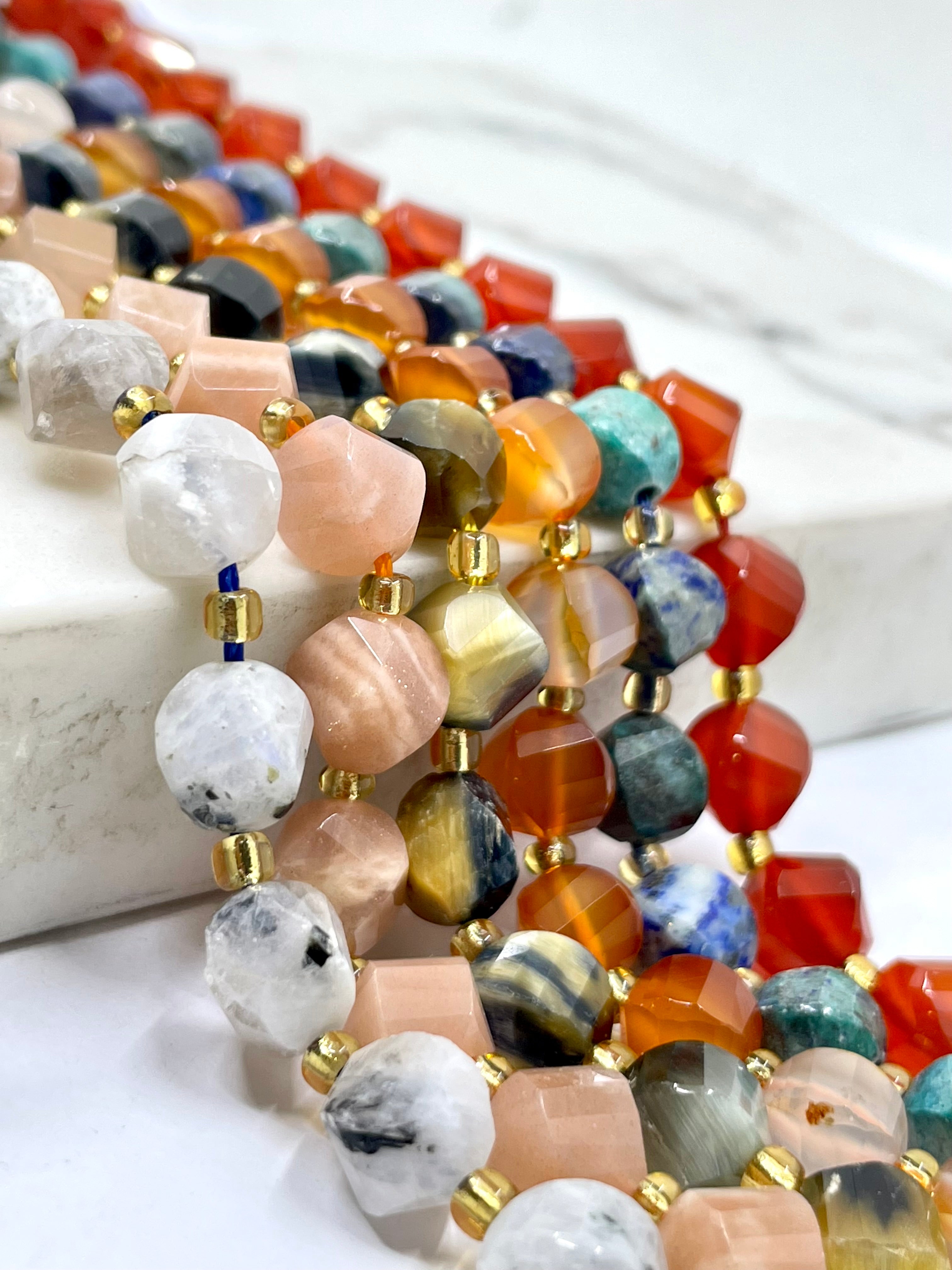 Close-up of a strand of multicolor gemstone beads with gold spacer beads, draped over a white marble block.